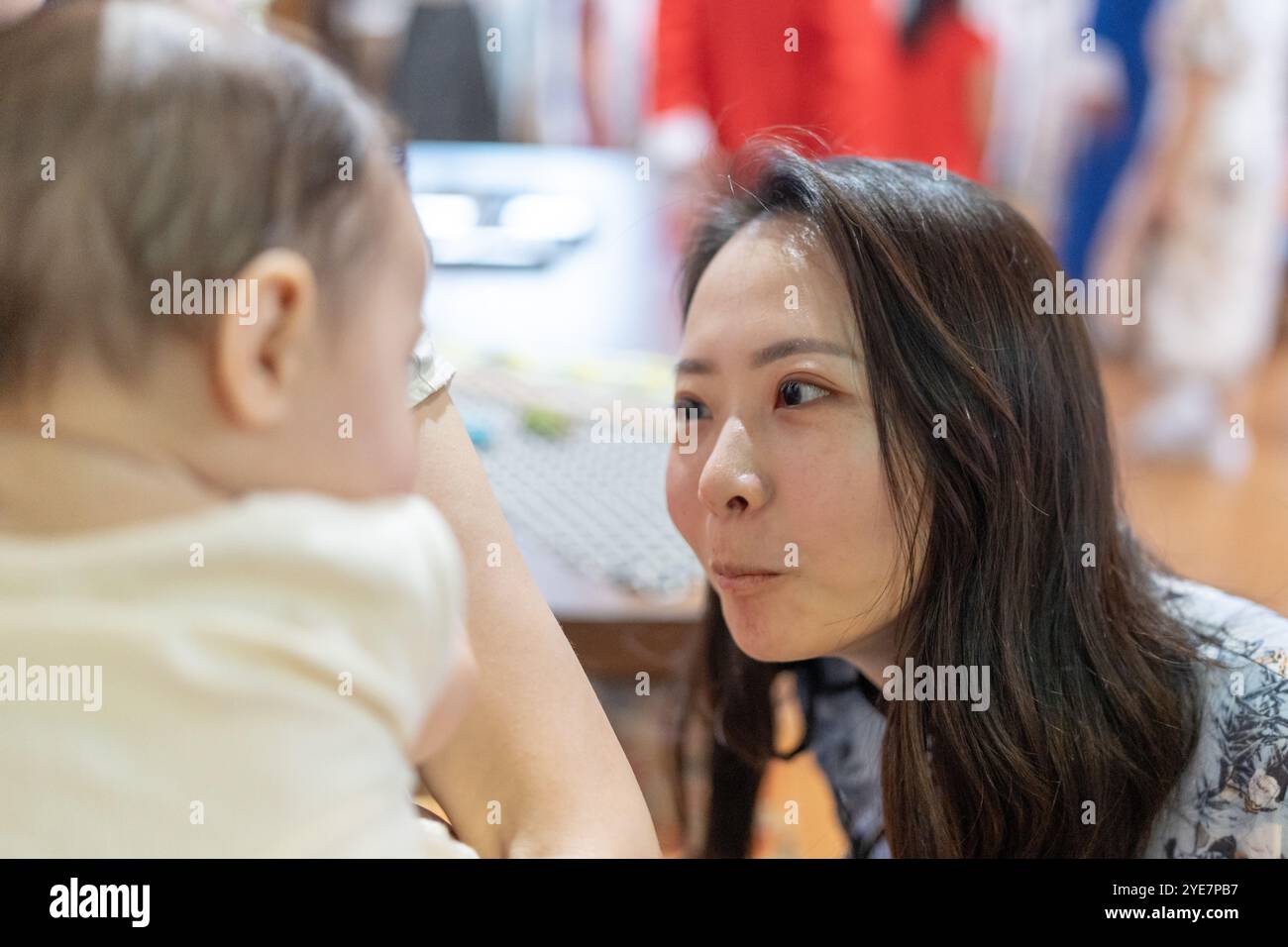Eine taiwanesische Frau im Alter von 30 Jahren in traditioneller chinesischer Kleidung unterhält ein 6 Monate altes Baby, das von einer anderen Frau in der Dihua Street in Ta festgehalten wird Stockfoto