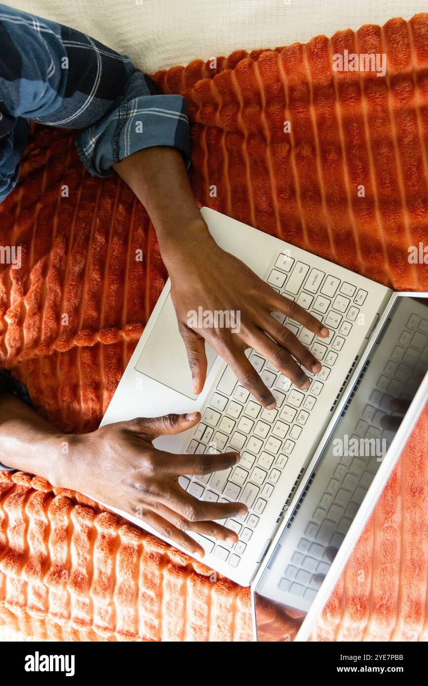 Auf Laptop tippen, afroamerikaner, der von zu Hause aus auf einer gemütlichen orangen Decke arbeitet Stockfoto