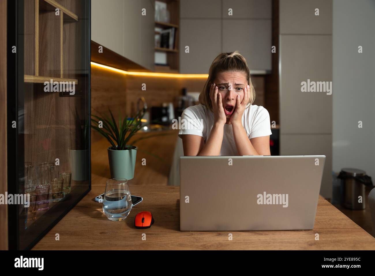 Die junge unzufriedene, verwirrte junge blonde Geschäftsfrau im Home Office arbeitet mit Dokumenten und Laptop-Computer. Negative Online-Überraschung für Fre Stockfoto