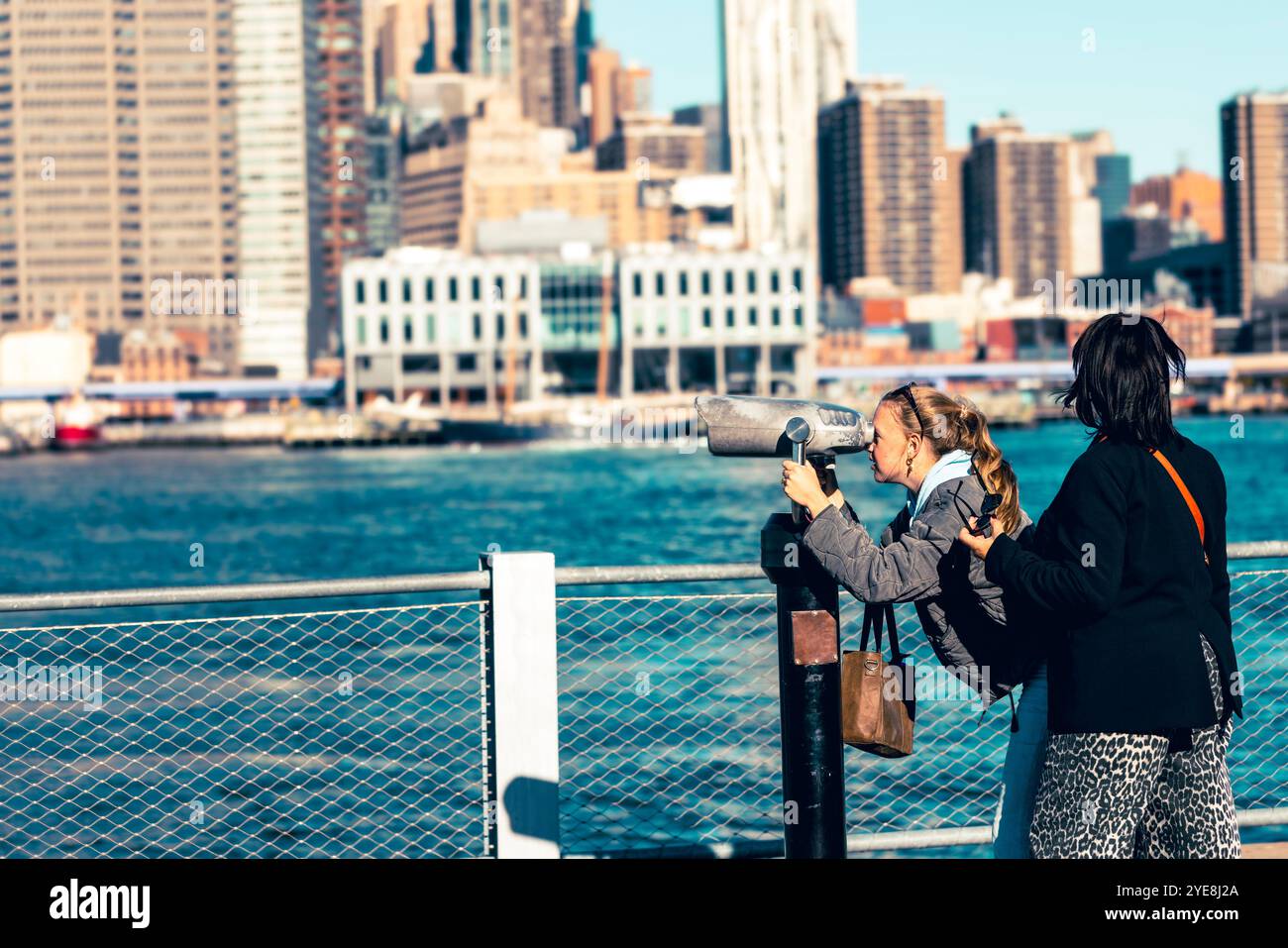 Ein Mädchen und ihre Mutter betrachten Downtown Manhattan durch Ferngläser in einem Park: Ein herzerwärmender Moment, in dem sie ihre gemeinsame Neugier einfangen Stockfoto
