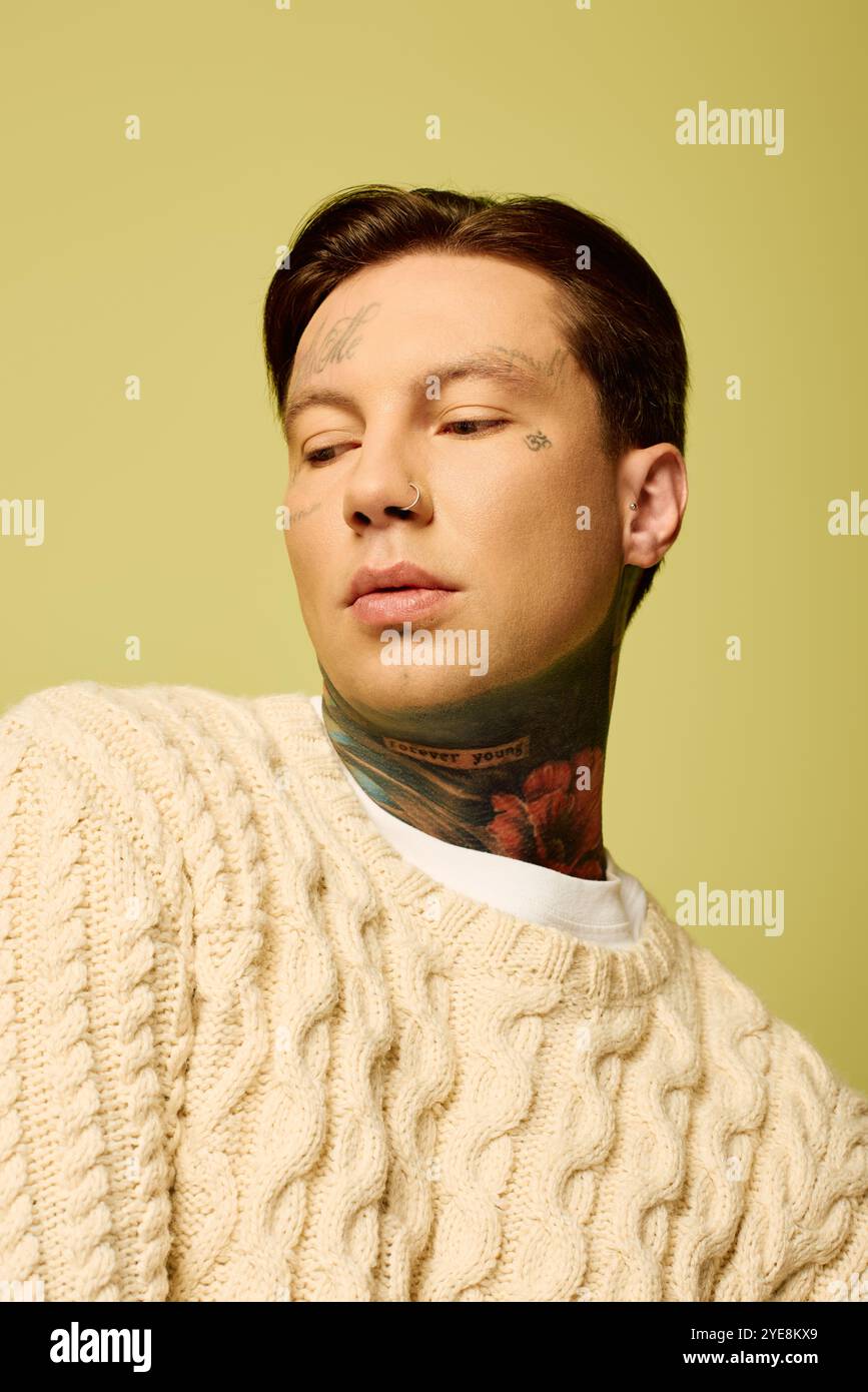 Ein junger Mann, der mit komplizierten Tattoos geschmückt ist, zeigt einen kontemplativen Ausdruck in einer warmen Umgebung. Stockfoto