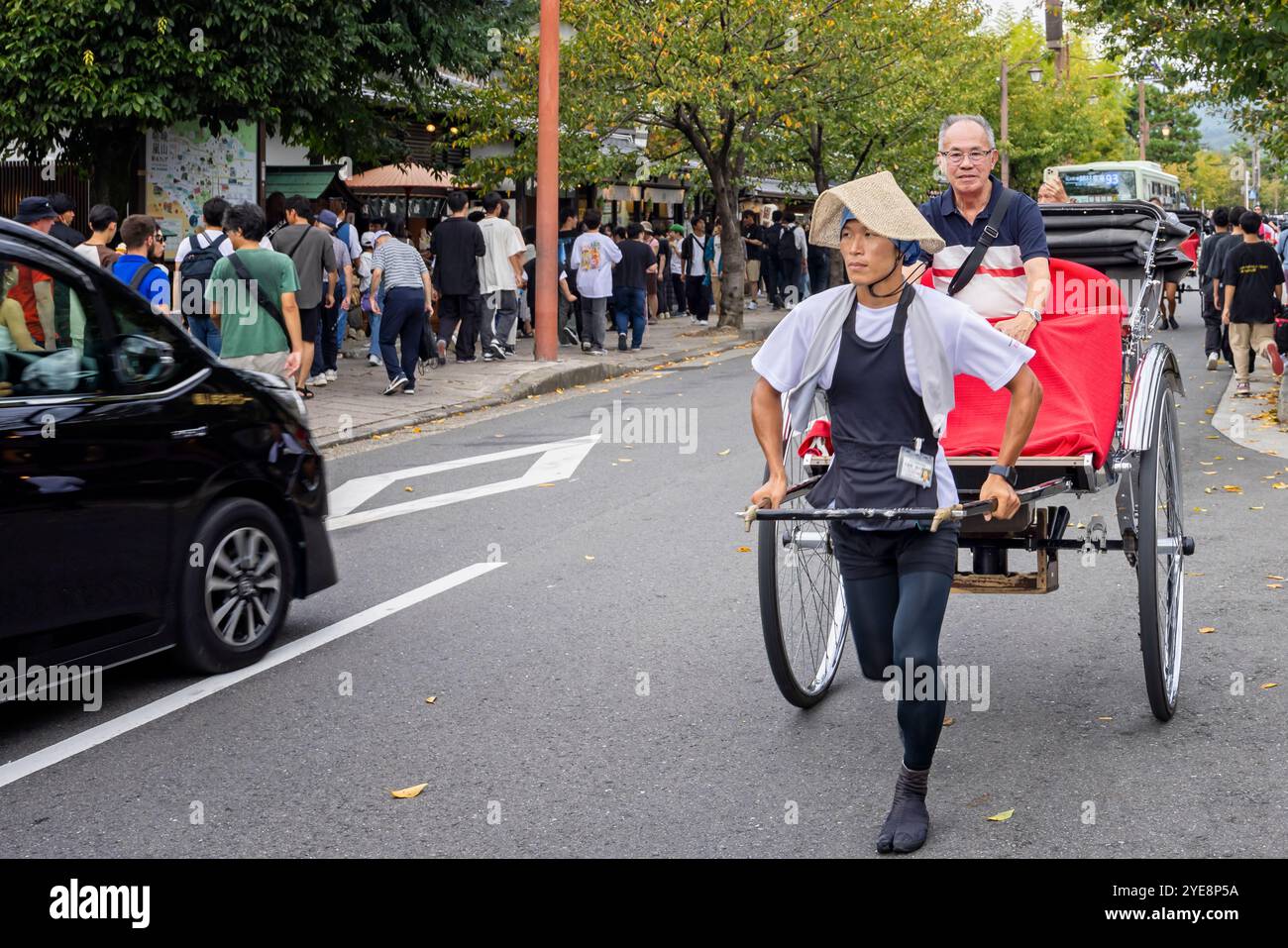 Ein junger japanischer Mann, der am 28. September 2024 eine Rikscha mit Passagier an Bord durch die Straßen von Arashiyama zog Stockfoto