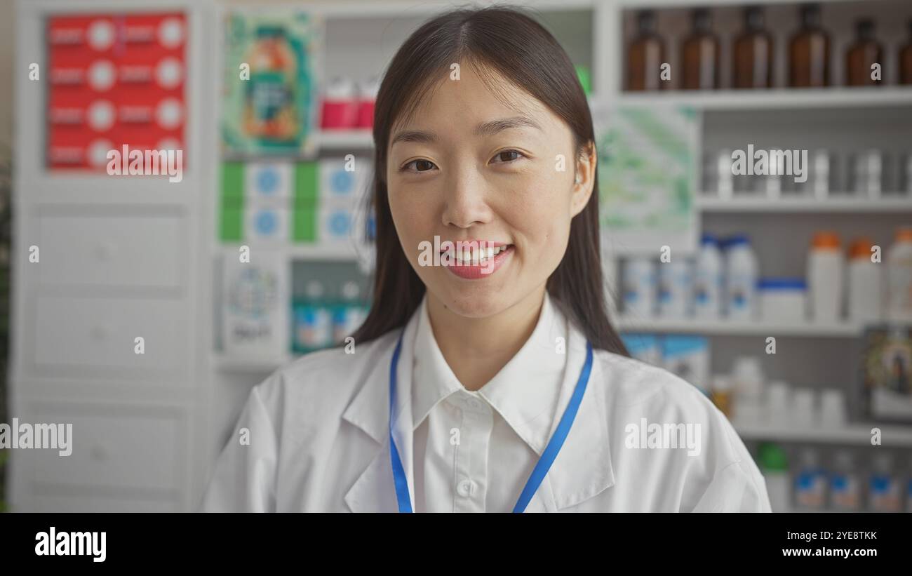 Eine fröhliche junge asiatische Apothekerin, die in einer modernen Drogerie steht und selbstbewusst in die Kamera lächelt. Stockfoto