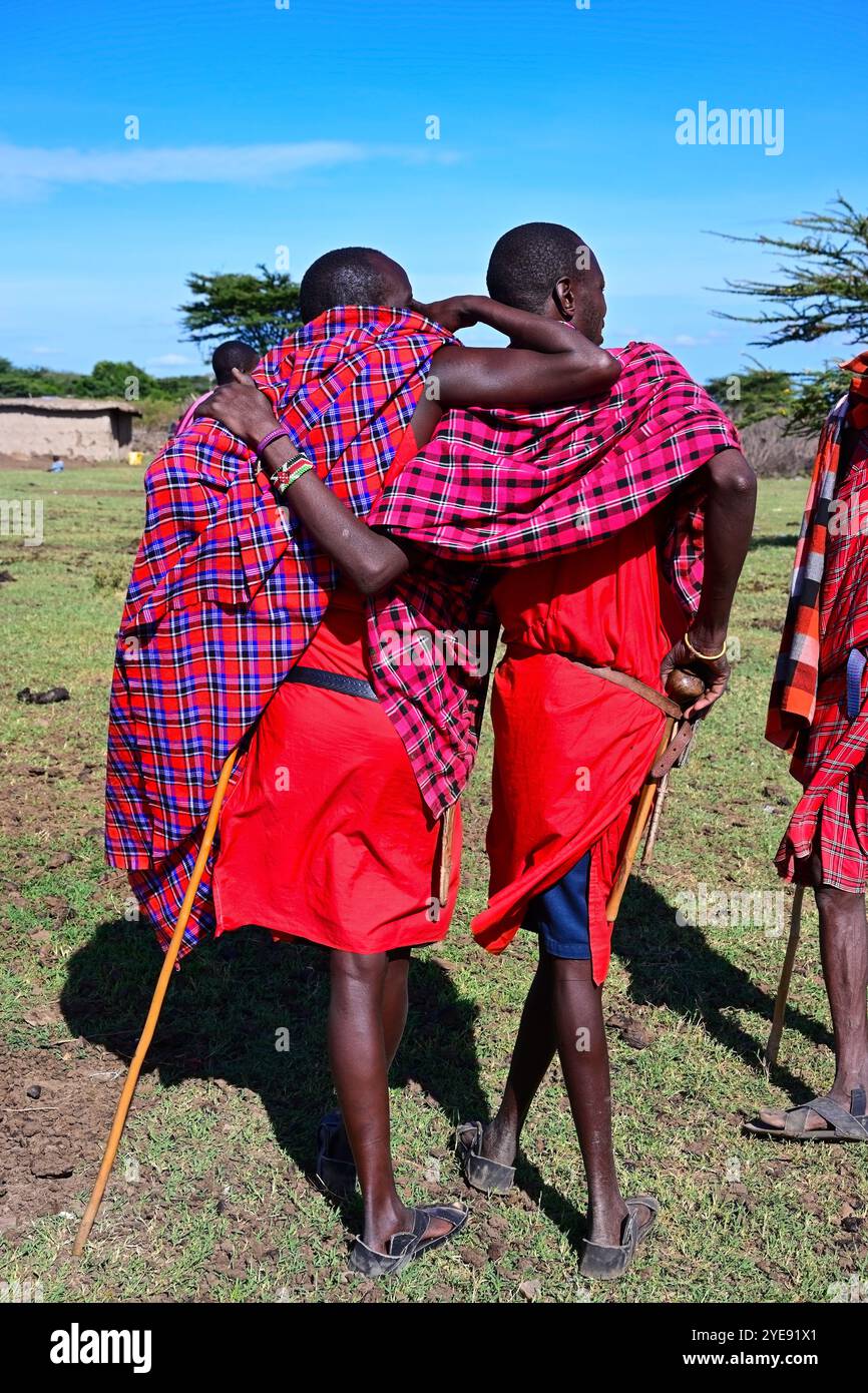 MAASAI MARA NATIONAL RESERVE, KENIA, AFRIKA - 11. NOVEMBER 2022: Maasai-Männer in traditioneller heller Kleidung stehen mitten in einem Maasai-Dorf in K Stockfoto