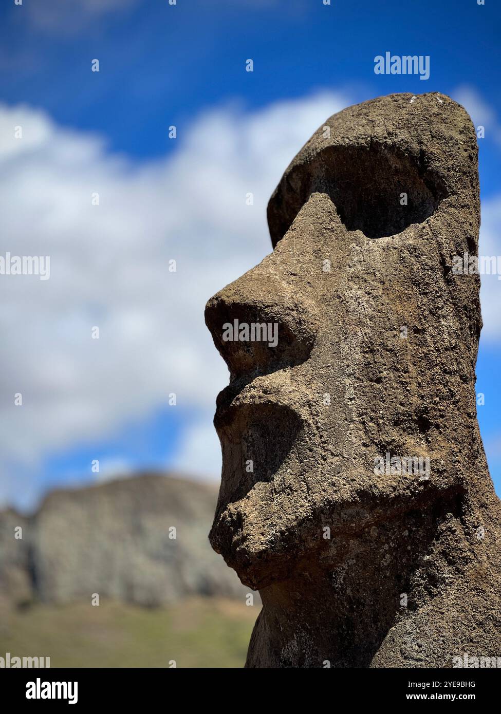 Nahaufnahme einer Moai-Statue auf der Osterinsel, Chile, mit detaillierten Steinelementen vor einer verschwommenen Bergkulisse und blauem Himmel. Stockfoto