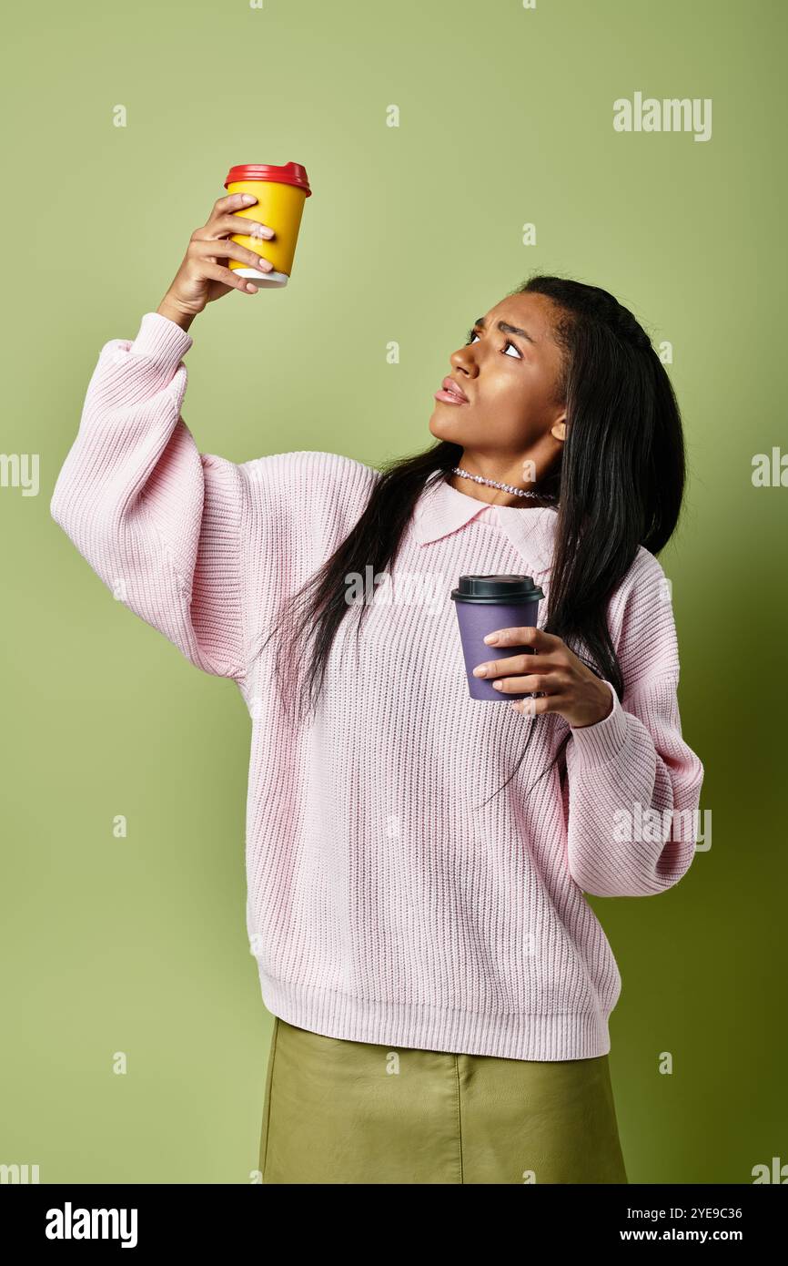Eine modische junge Frau hält zwei warme Getränke und blickt neugierig nach oben. Stockfoto