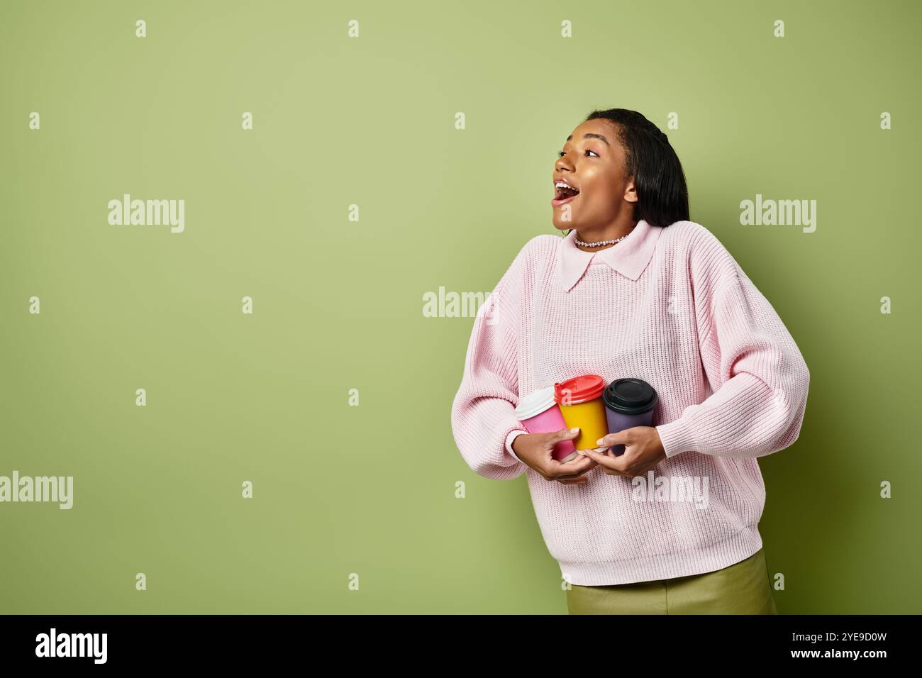 Die junge Frau hält fröhlich mehrere warme Getränke, stilvoll für das Herbstwetter gekleidet. Stockfoto