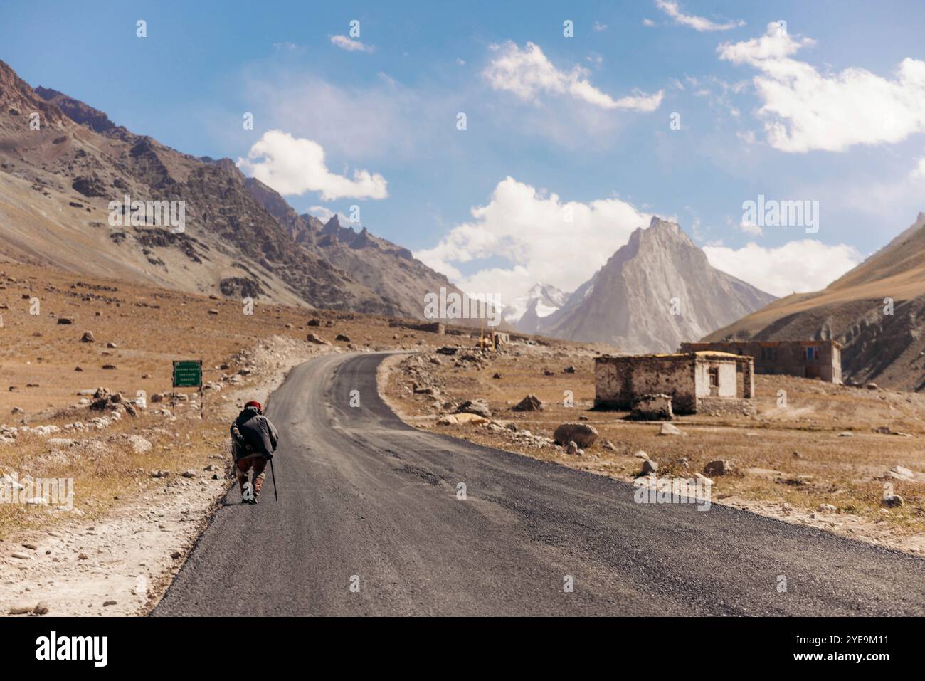 Senior man läuft mit einem Stock auf einer Asphaltstraße in der Nähe von Kurgiakh im Zanskar-Tal, Ladakh, Indien; Zanskar-Tal, Ladakh, Indien Stockfoto