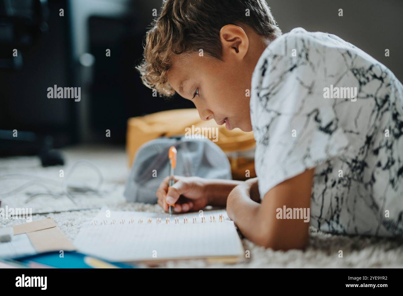 Ein konzentrierter Junge, der Hausaufgaben macht, während er zu Hause vorne liegt Stockfoto