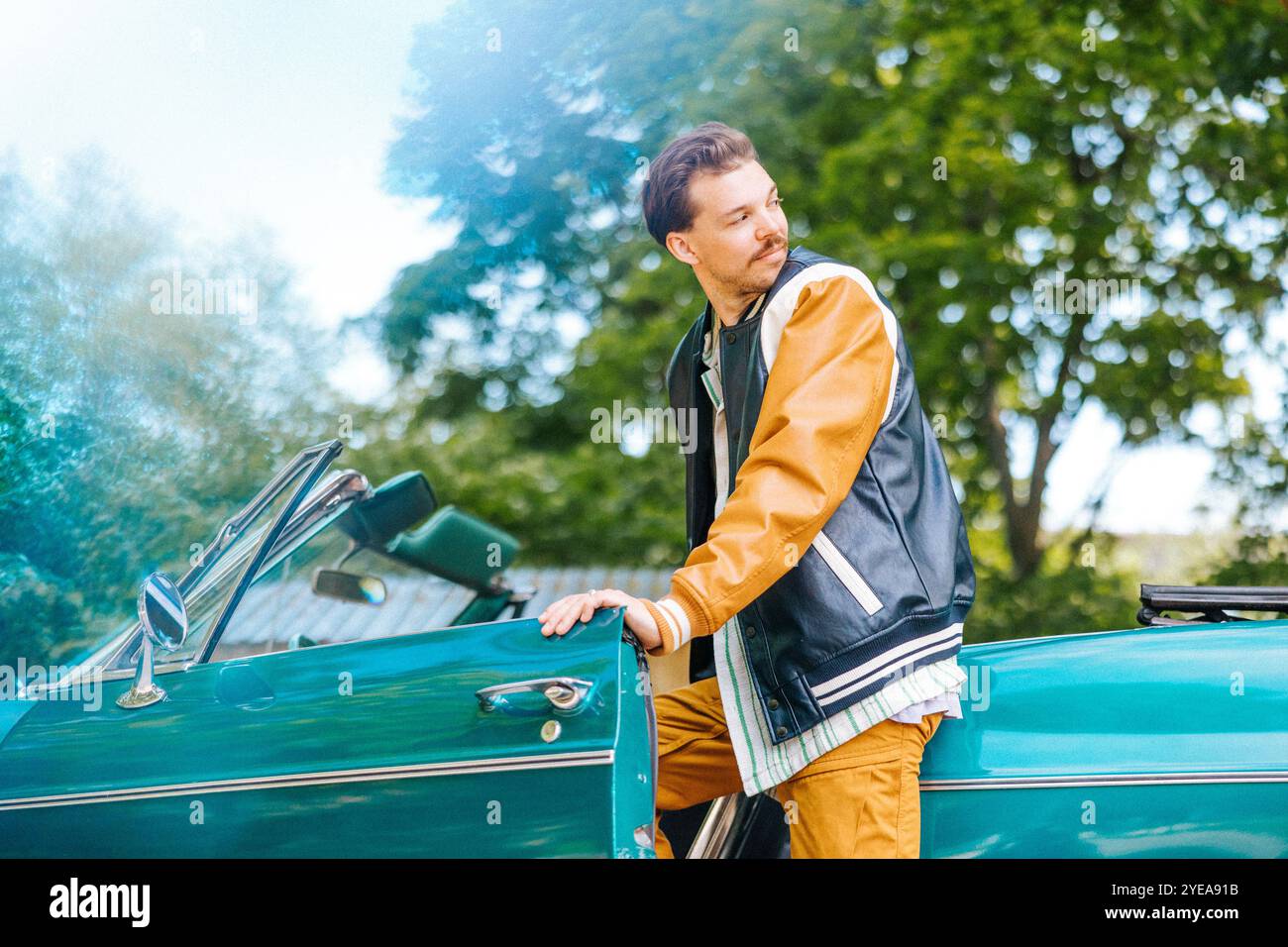 Junger Mann, der über die Schulter schaut, während er an sonnigem Tag ins Auto steigt Stockfoto