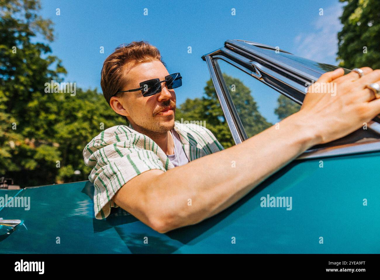 Tiefwinkelansicht eines jungen Mannes mit tätowiertem Arm, der Sonnenbrille trägt, während er im Oldtimer sitzt Stockfoto