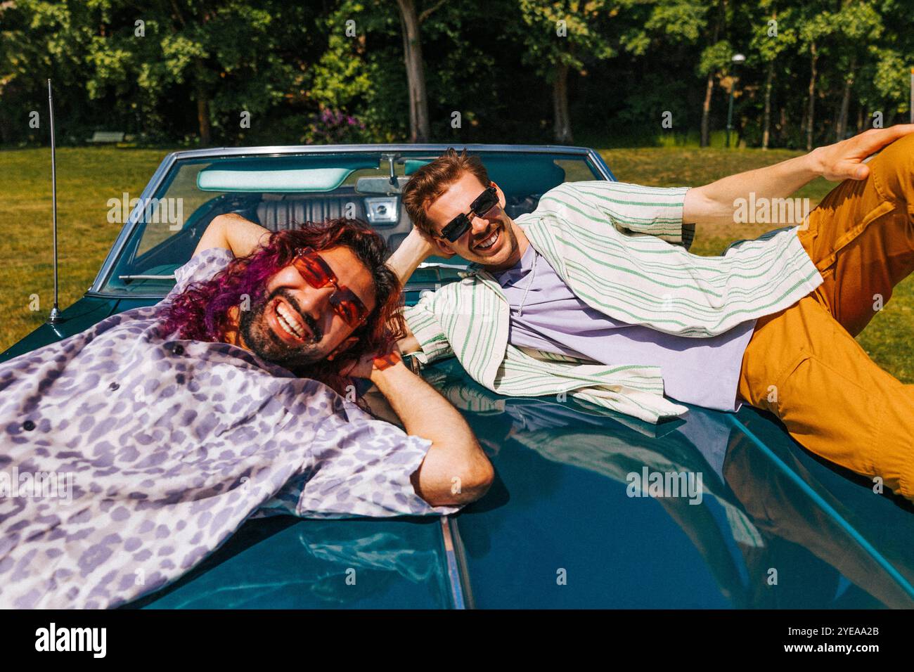 Porträt glücklicher, multirassischer männlicher Freunde, die am sonnigen Tag auf einem Oldtimer im Park liegen Stockfoto