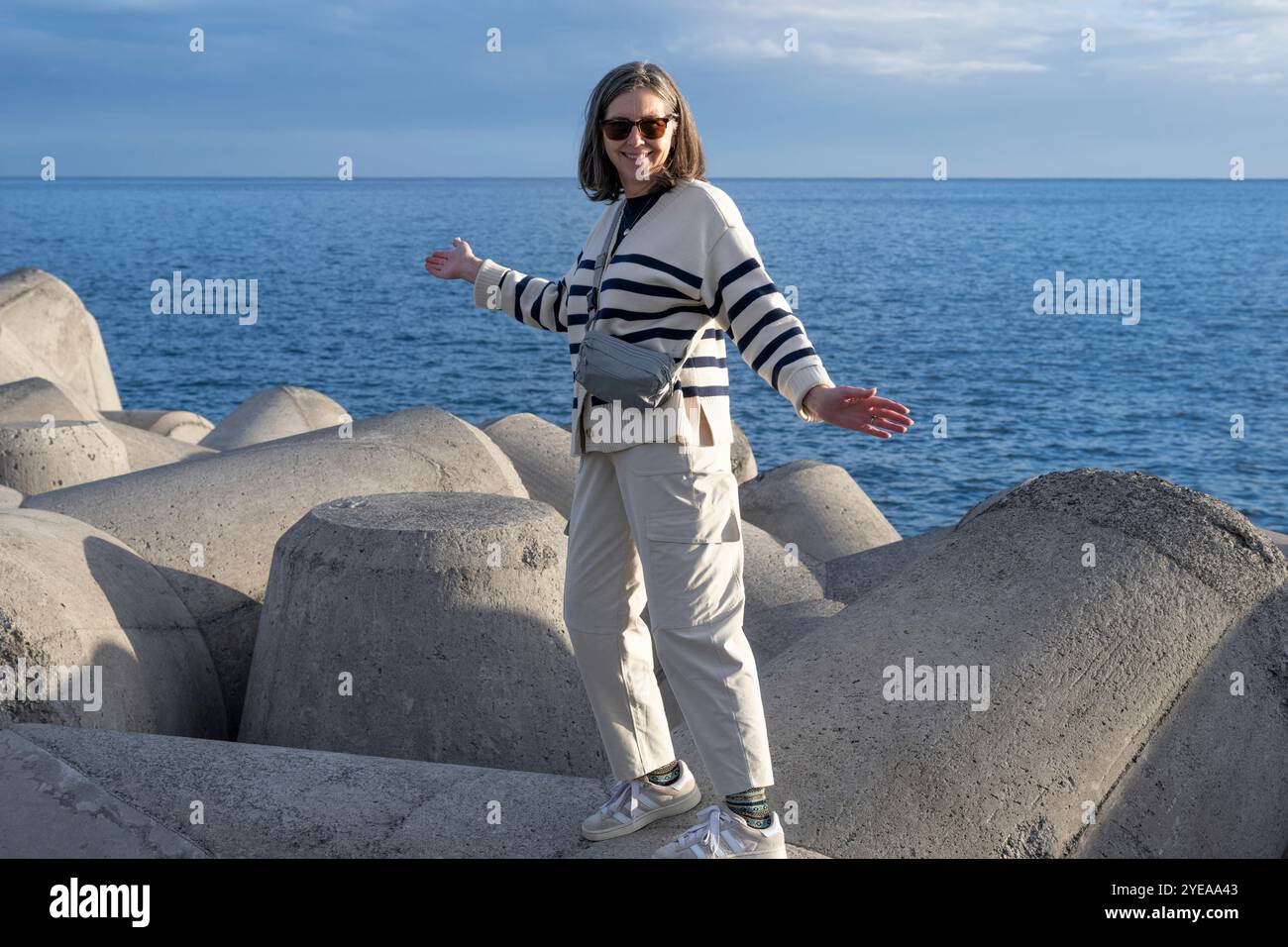 Frau mit Sonnenbrille posiert im Sonnenlicht entlang Betonbauten an der Uferpromenade von Funchal auf Madeira, Portugal Stockfoto