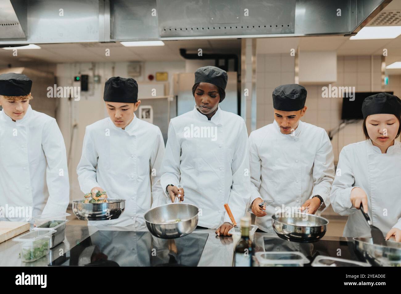 Männliche und weibliche Auszubildende mit Kochtöpfen in der Kochschule Stockfoto