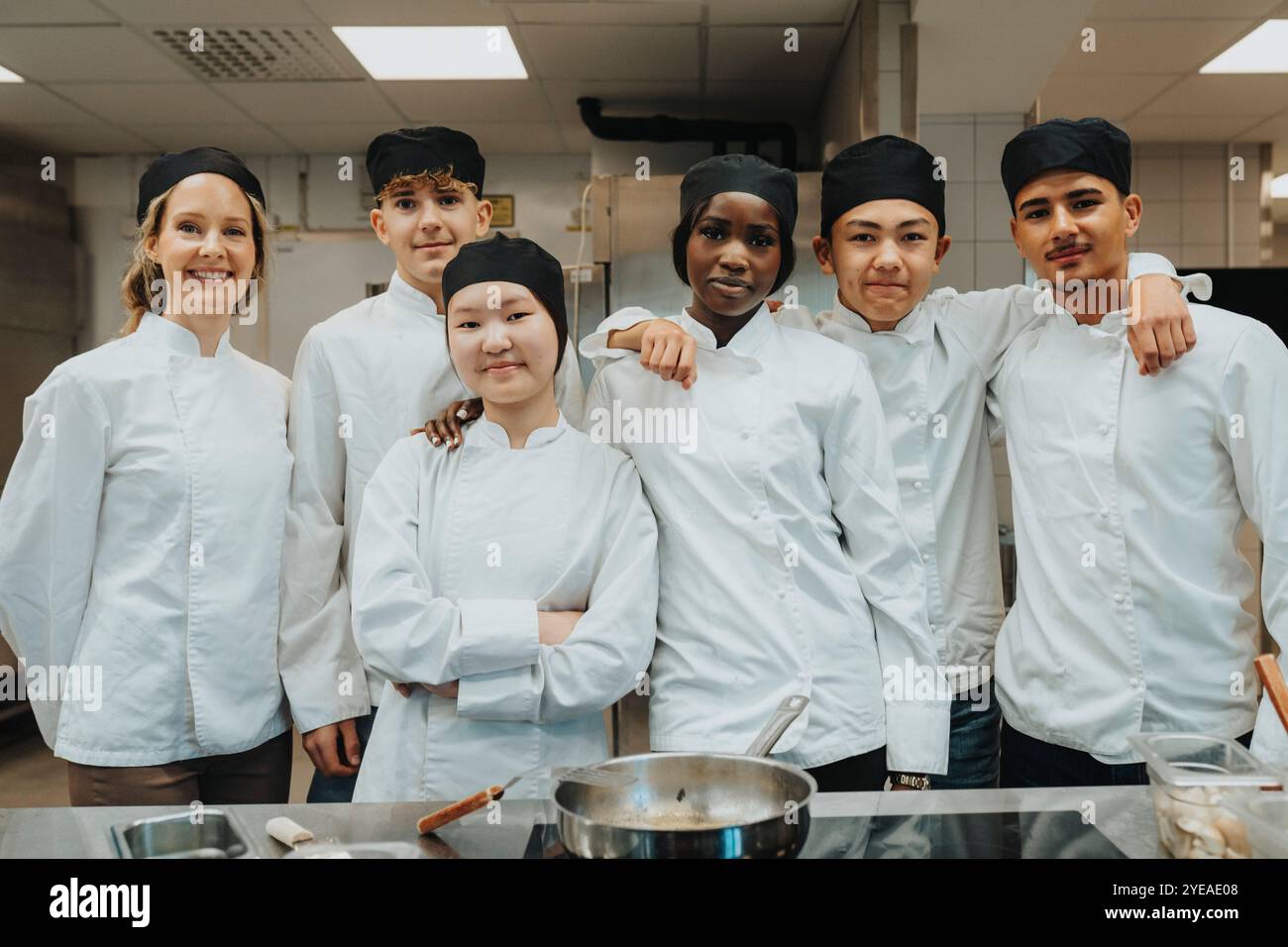 Porträt von männlichen und weiblichen Auszubildenden, die mit dem Lehrer in der Handelsküche stehen Stockfoto