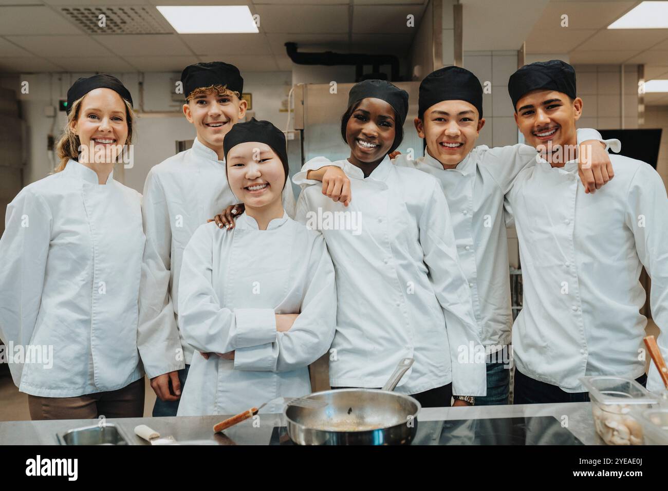 Porträt eines glücklichen männlichen und weiblichen Auszubildenden, der mit dem Lehrer an der Restauranthochschule steht Stockfoto