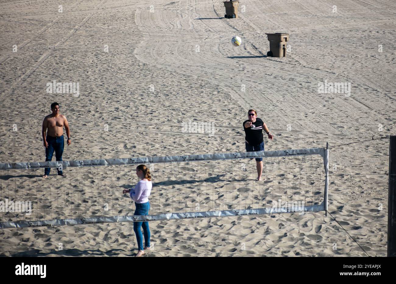 Ungezwungene Beachvolleyballspieler, die den Tag genießen und die Leute mit dem Ball auf dem Sand beobachten Stockfoto