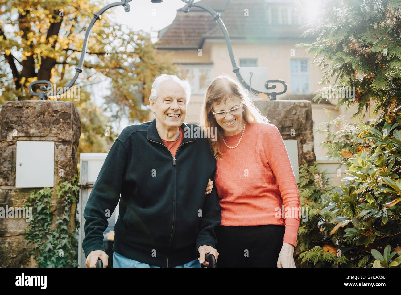 Glückliche ältere Frau mit Seniorenmann, der mit Hilfe eines Mobilitätsgehers läuft Stockfoto