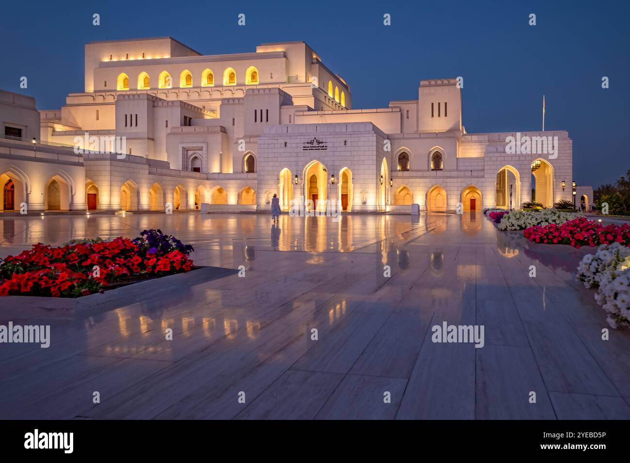 Das Royal Opera House Muscat ist nachts wunderschön beleuchtet und spiegelt sich elegant auf polierten Böden wider. Stockfoto