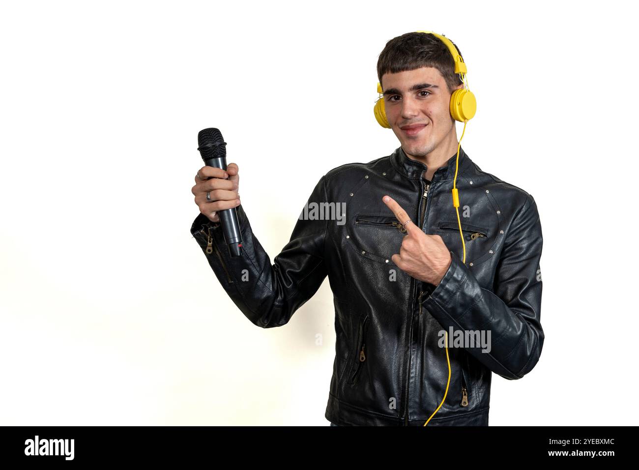 Junger Erwachsener mit Mikrofon, der mit gelben Kopfhörern auf weißem Hintergrund Musik hört Stockfoto