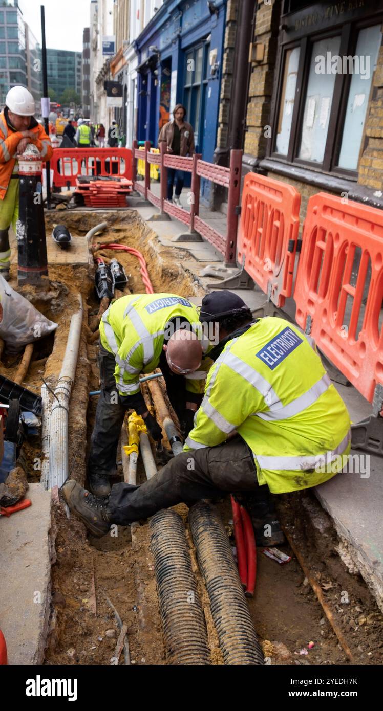 Arbeiter, die an Stromkabeln arbeiten, die unter dem Bürgersteig in der Smithfield Charterhouse Street London, England, graben, KATHY DEWITT Stockfoto