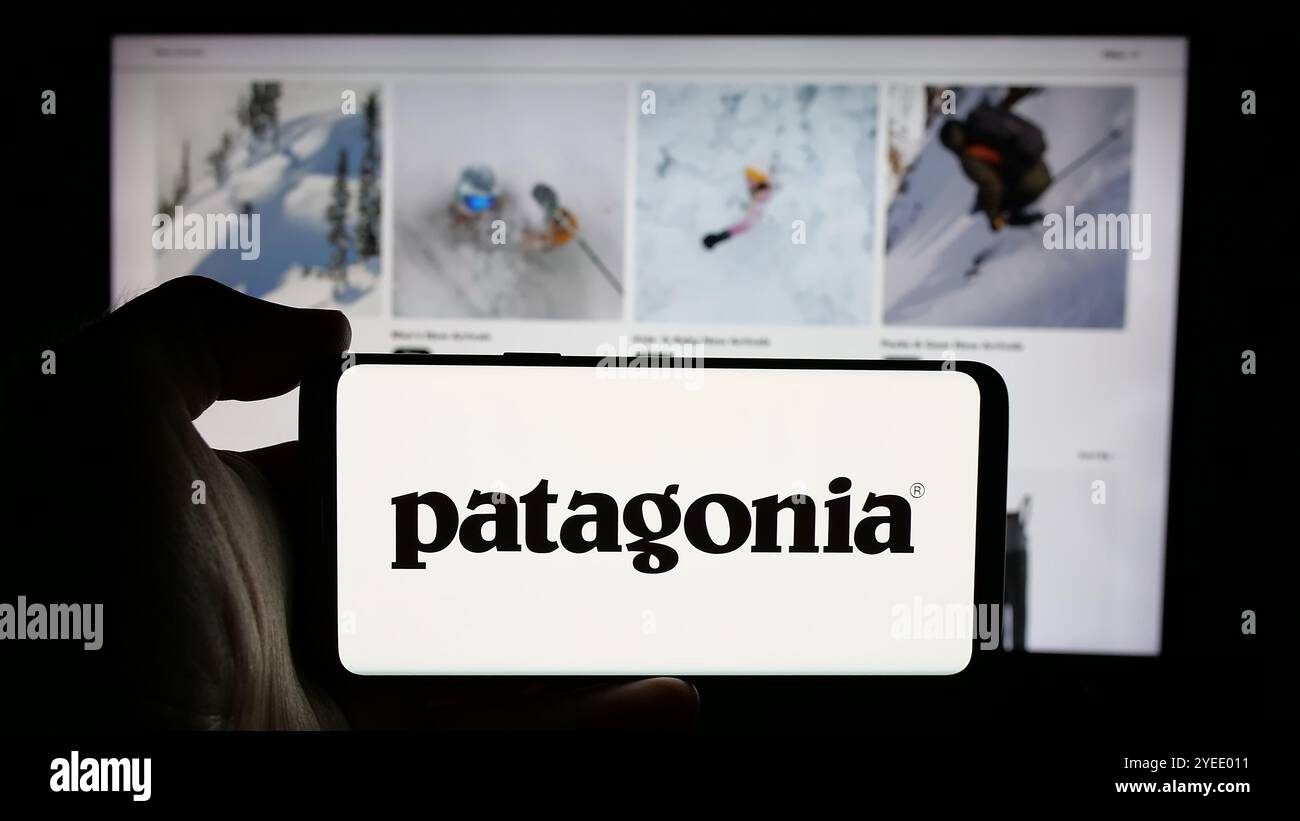 Person, die ein Mobiltelefon mit dem Logo des US-amerikanischen Outdoor-Bekleidungsunternehmens Patagonia Inc. Auf dem Bildschirm vor der Business-Website hält. Schwerpunkt auf dem Display des Telefons. Stockfoto
