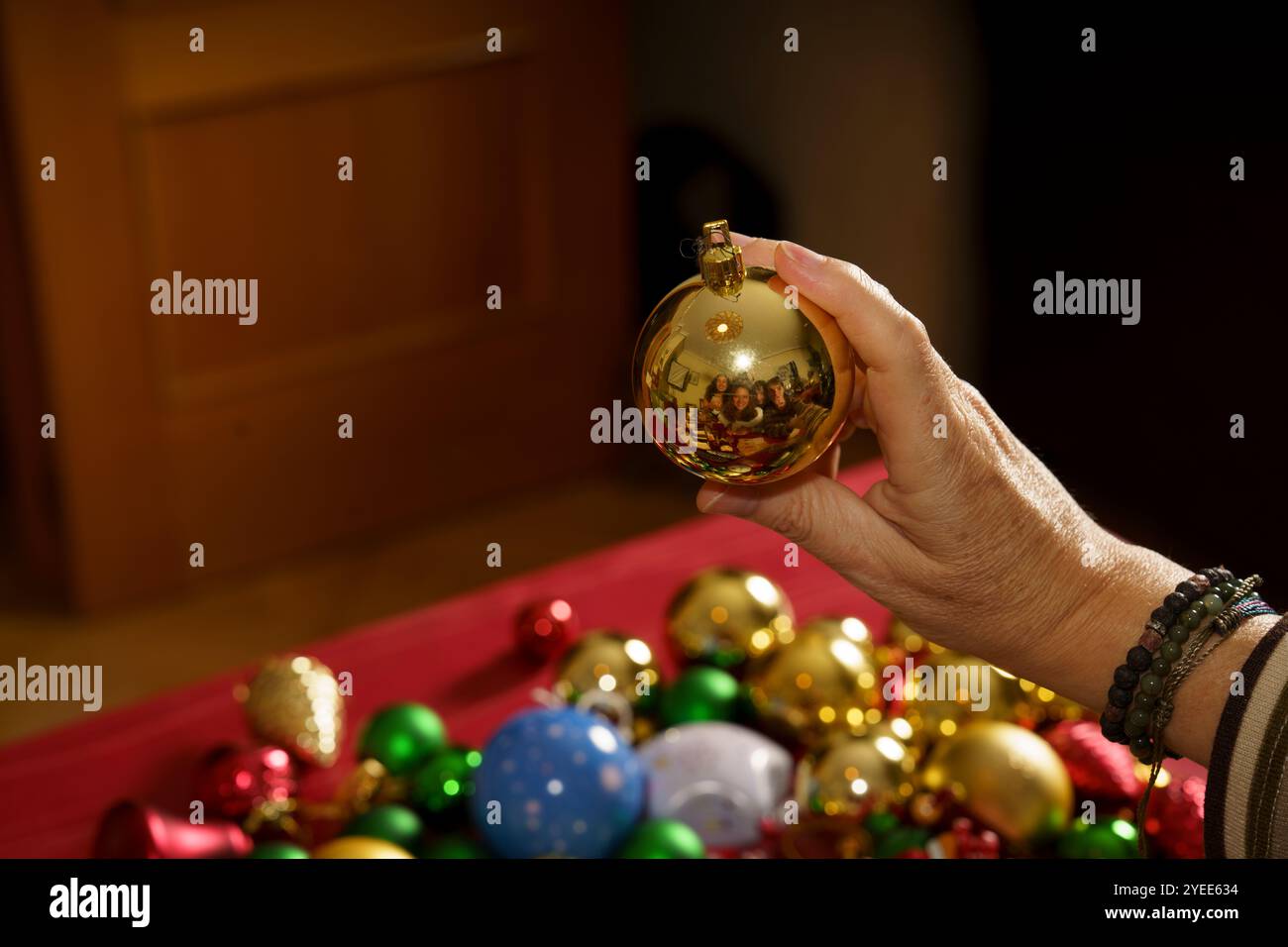 Eine Person hält ein goldenes Ornament mit einer grünen und blauen Kugel drauf. Die Szene ist auf einem Tisch mit vielen anderen Ornamenten inszeniert Stockfoto