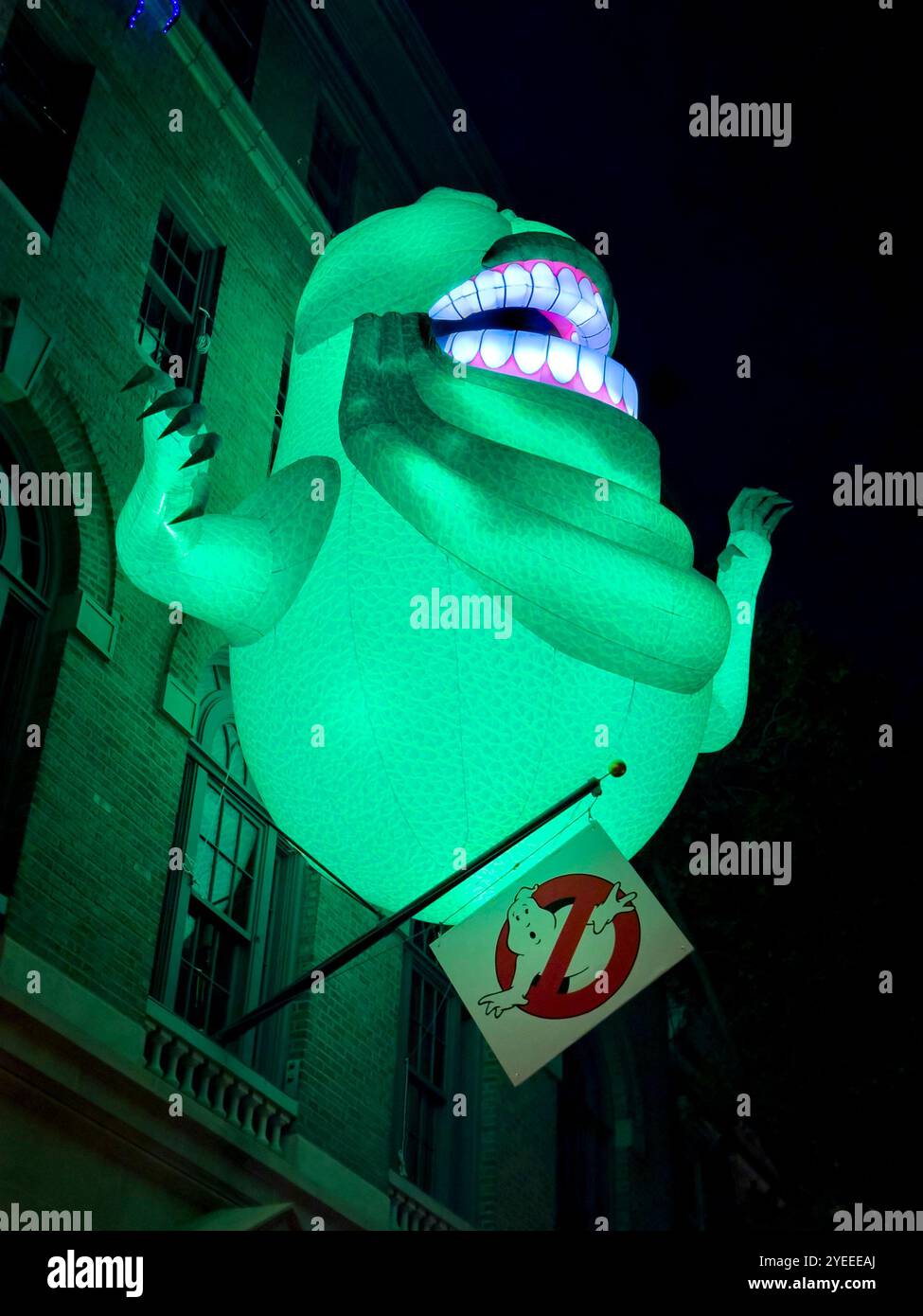 Große beleuchtete Installation einer grünen Zeichentrickfigur über einem historischen Gebäude mit leuchtendem Grün und lächelndem Ausdruck - Smartphone-aufgenommenes Stockfoto