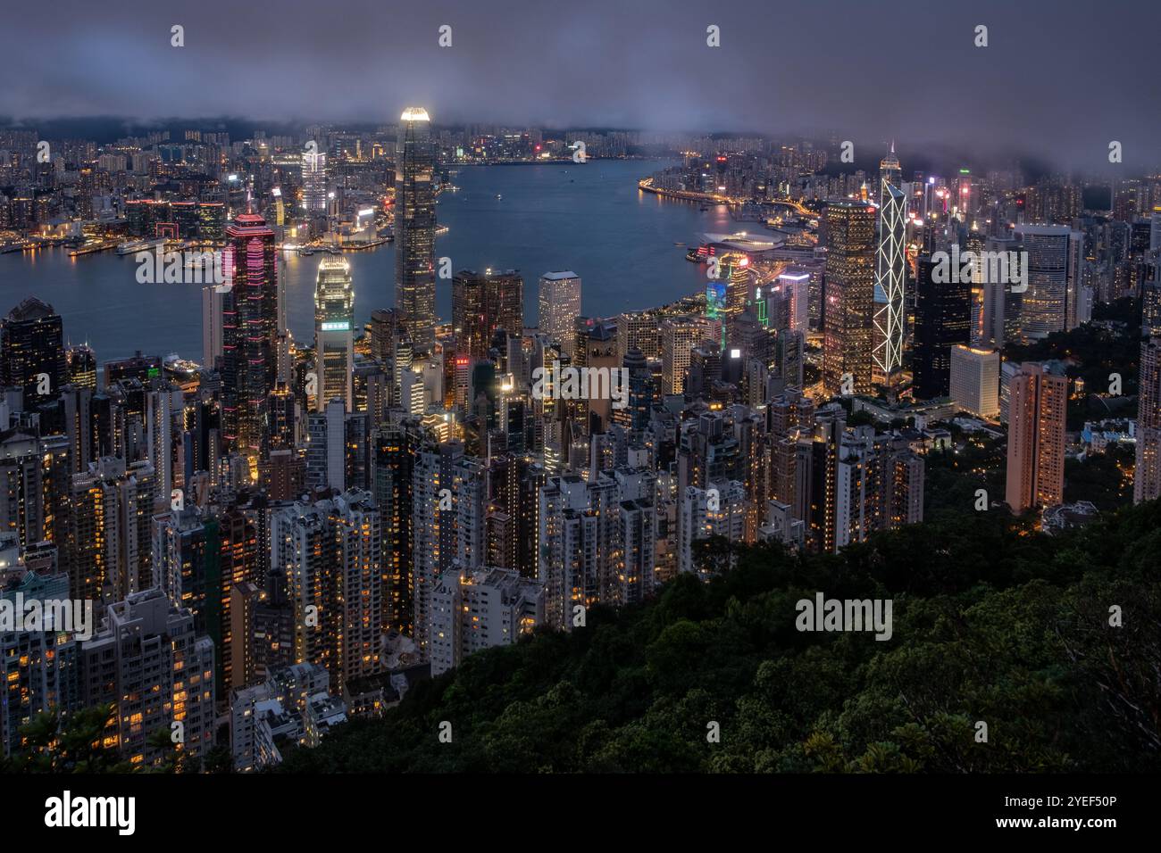 In der Abenddämmerung vom Peak entfaltet sich das atemberaubende Panorama des Victoria Harbour, mit der Skyline von Central und Kowloon, die gegen einen klaren Abend beleuchtet wird. Stockfoto