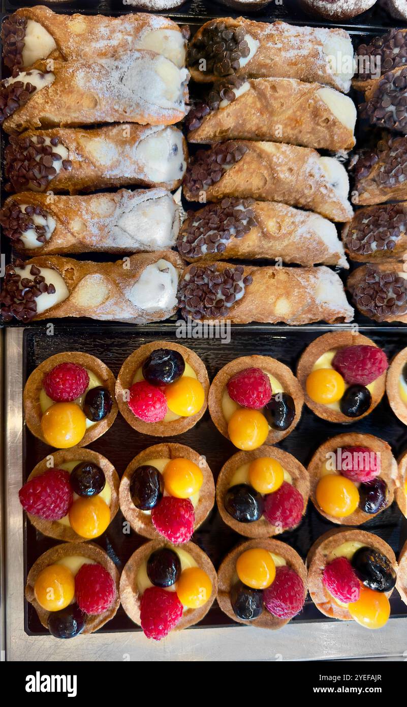 Eine Top-Down-Präsentation mit verschiedenen Backwaren, einschließlich Cannoli mit Schokoladenchips und Obstkuchen mit Himbeeren und goldenen Beeren Stockfoto