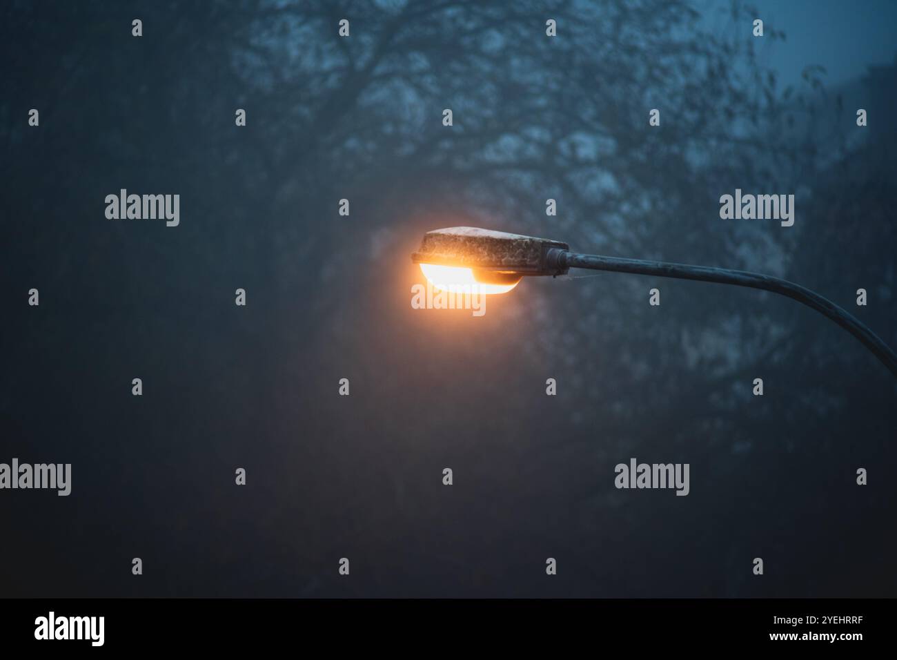 Trübe orange leuchtende Straßenlaterne an einem nebeligen Herbstabend. Moody-blaue Atmosphäre, keine Leute. Stockfoto