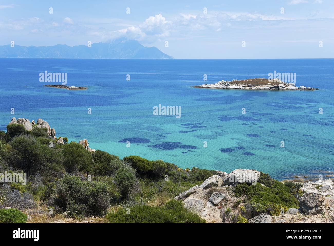 Atemberaubende Landschaft mit klarem türkisfarbenem Wasser und felsigen Inseln im Glanz der Sonne, Blick auf den Berg Athos, orthodoxe klosterrepublik mit Auton Stockfoto