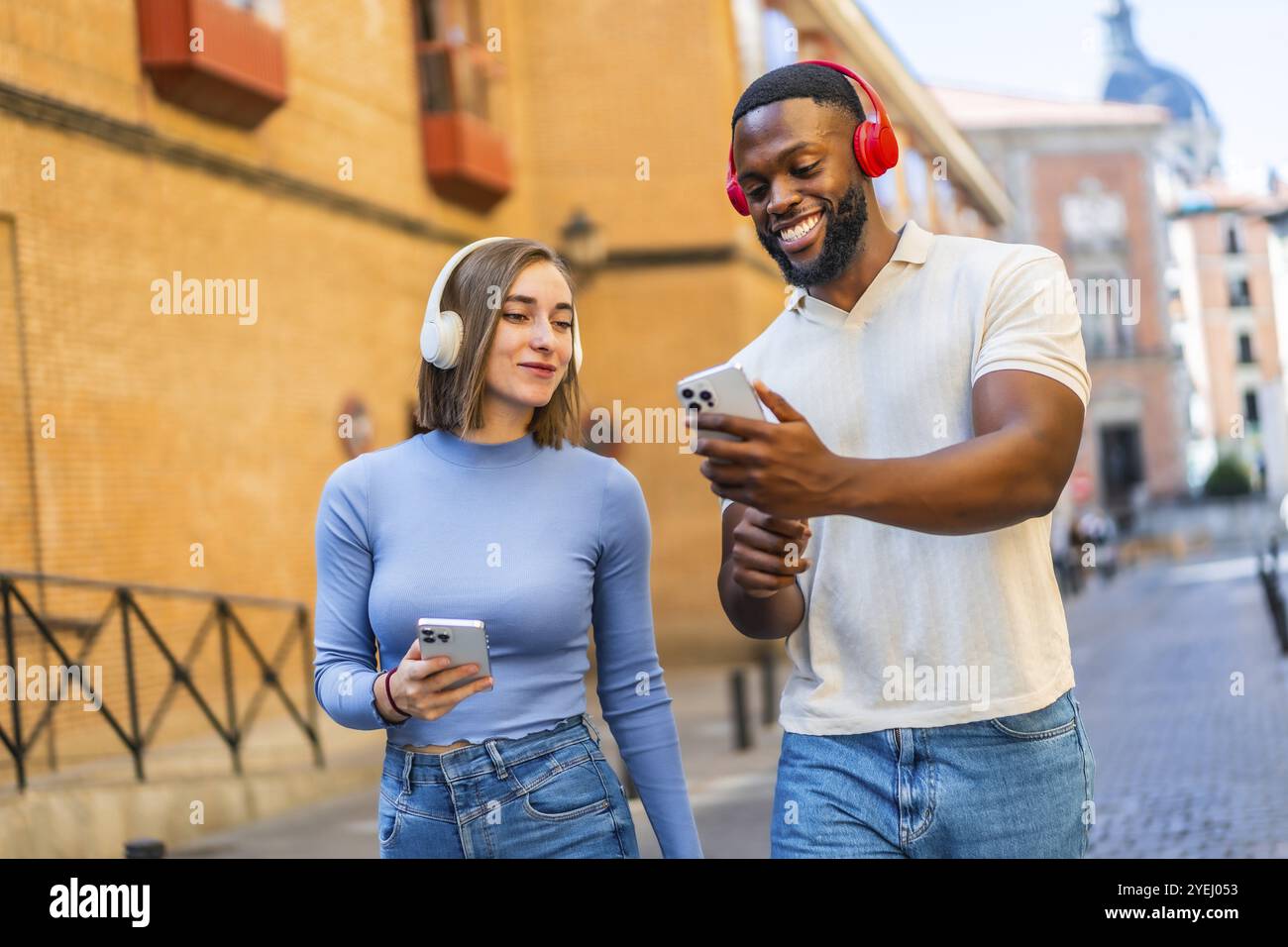 Multi-ethnische Paare, die in der Stadt über Mobiltelefon und Kopfhörer Inhalte teilen und lächeln Stockfoto