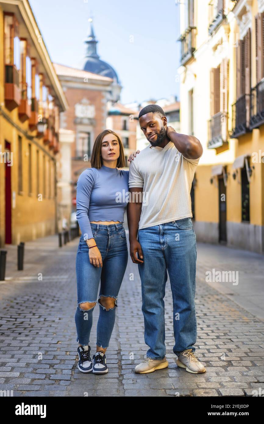 Vertikales Porträt eines multiethnischen Paares in Denim-Kleidung, das in der Stadt steht Stockfoto