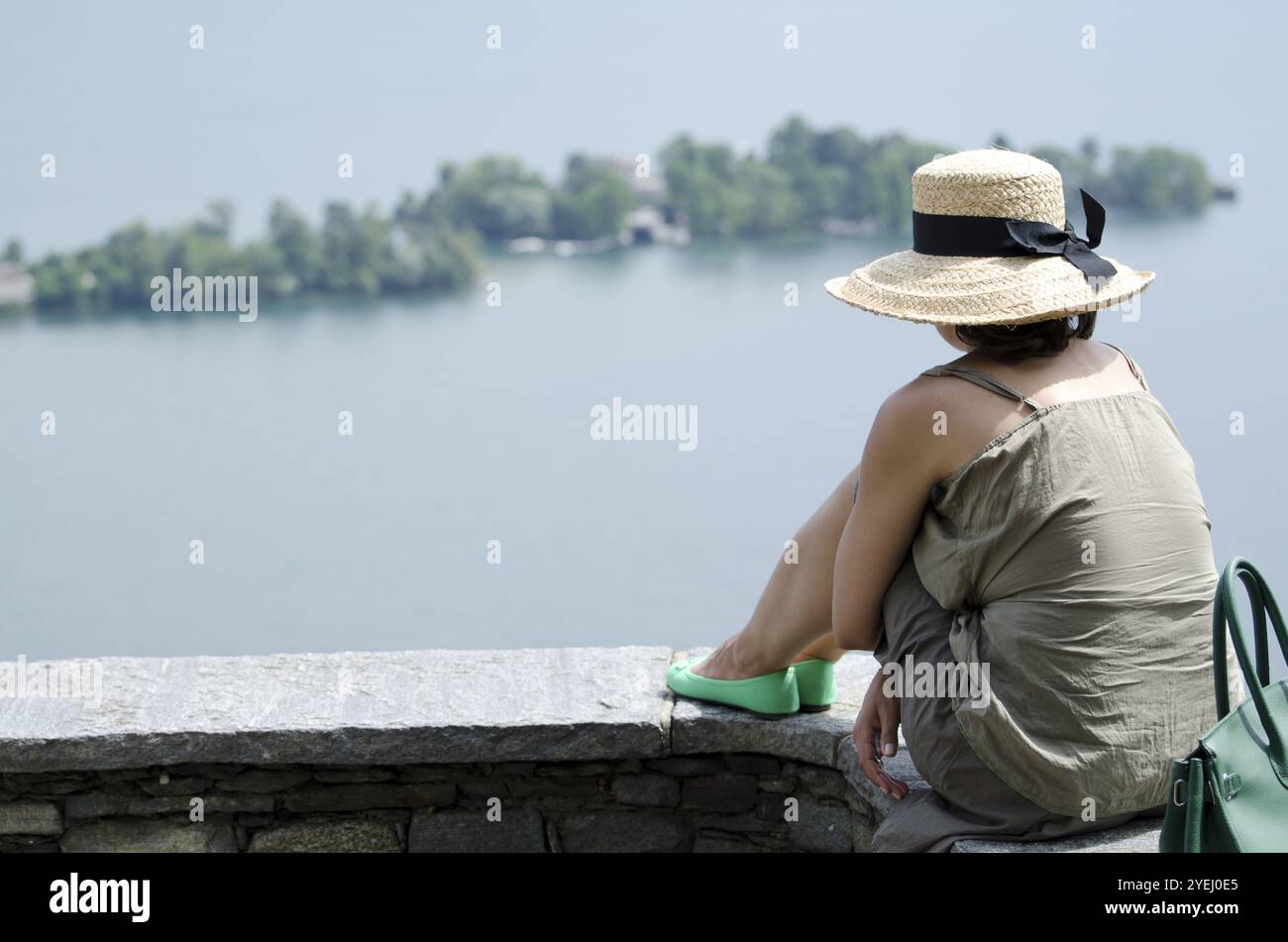 Frau, die auf einer Mauer sitzt und die Brissago-Inseln am Lago Maggiore in Ronco sopra Ascona, Tessin, Schweiz, Europa ansieht Stockfoto