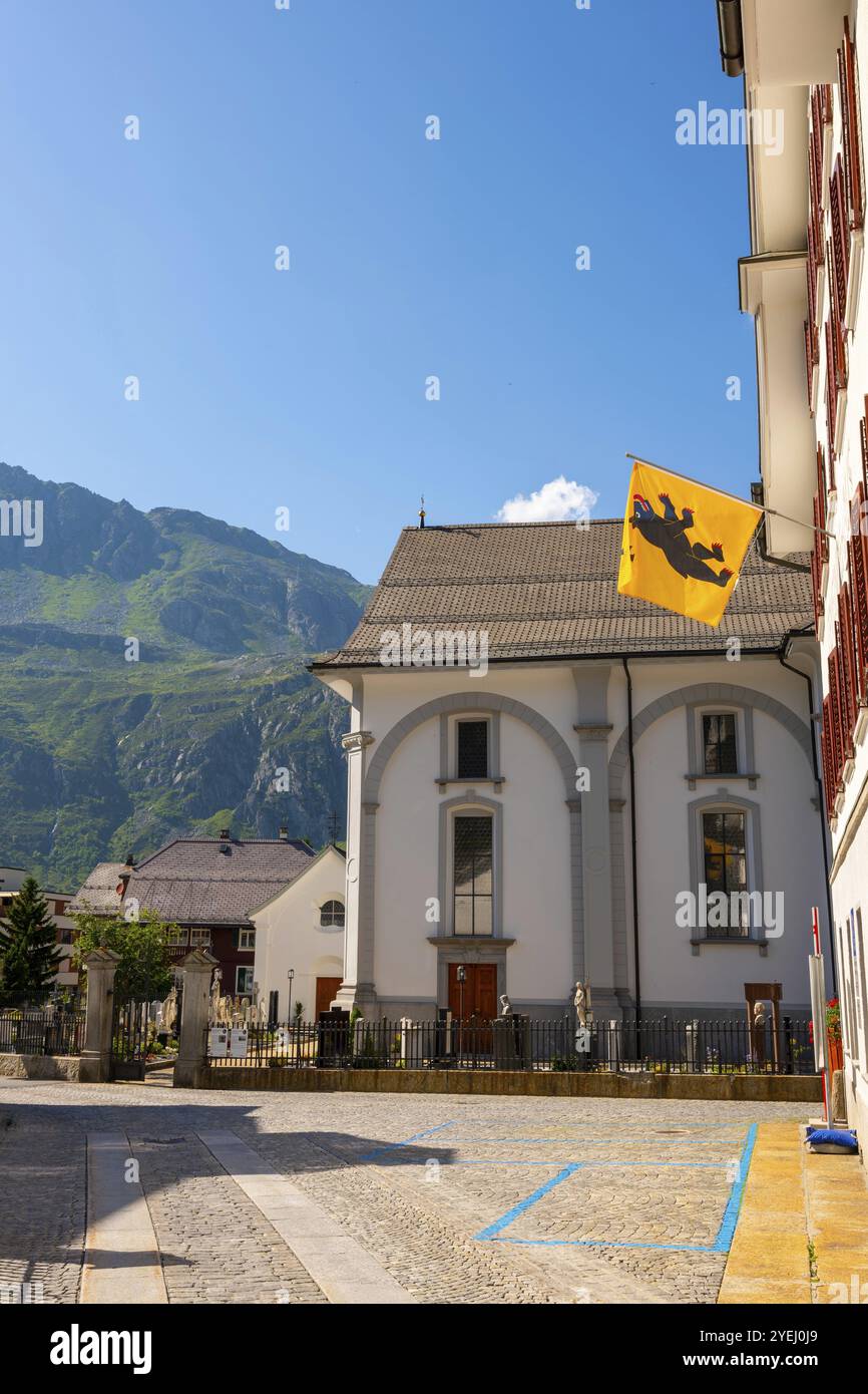 Wunderschöne katholische Pfarrkirche St. Peter und Paul in der Altstadt mit Berg und blauem Himmel an einem sonnigen Sommertag in Andermatt, URI, Schweiz, EUR Stockfoto