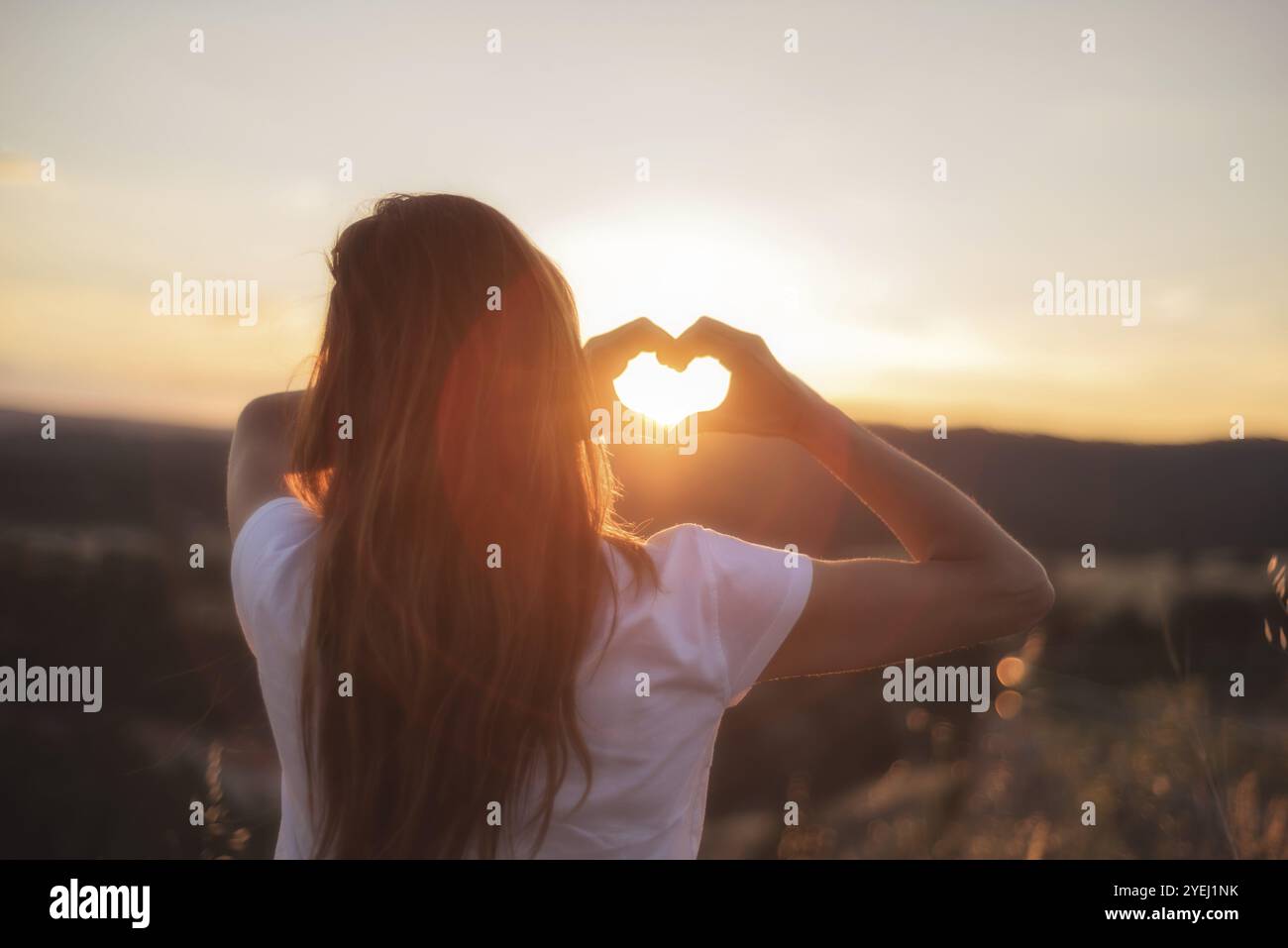 Liebeszeichen. Frau macht Herz mit ihren Händen bei Sonnenuntergang Stockfoto