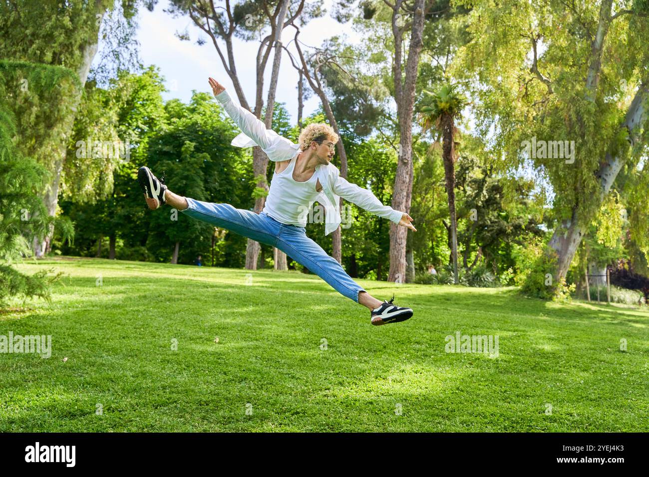 Junger Mann springt und tanzt zeitgenössisches Ballett im Park mit urbaner Tracht. Stockfoto