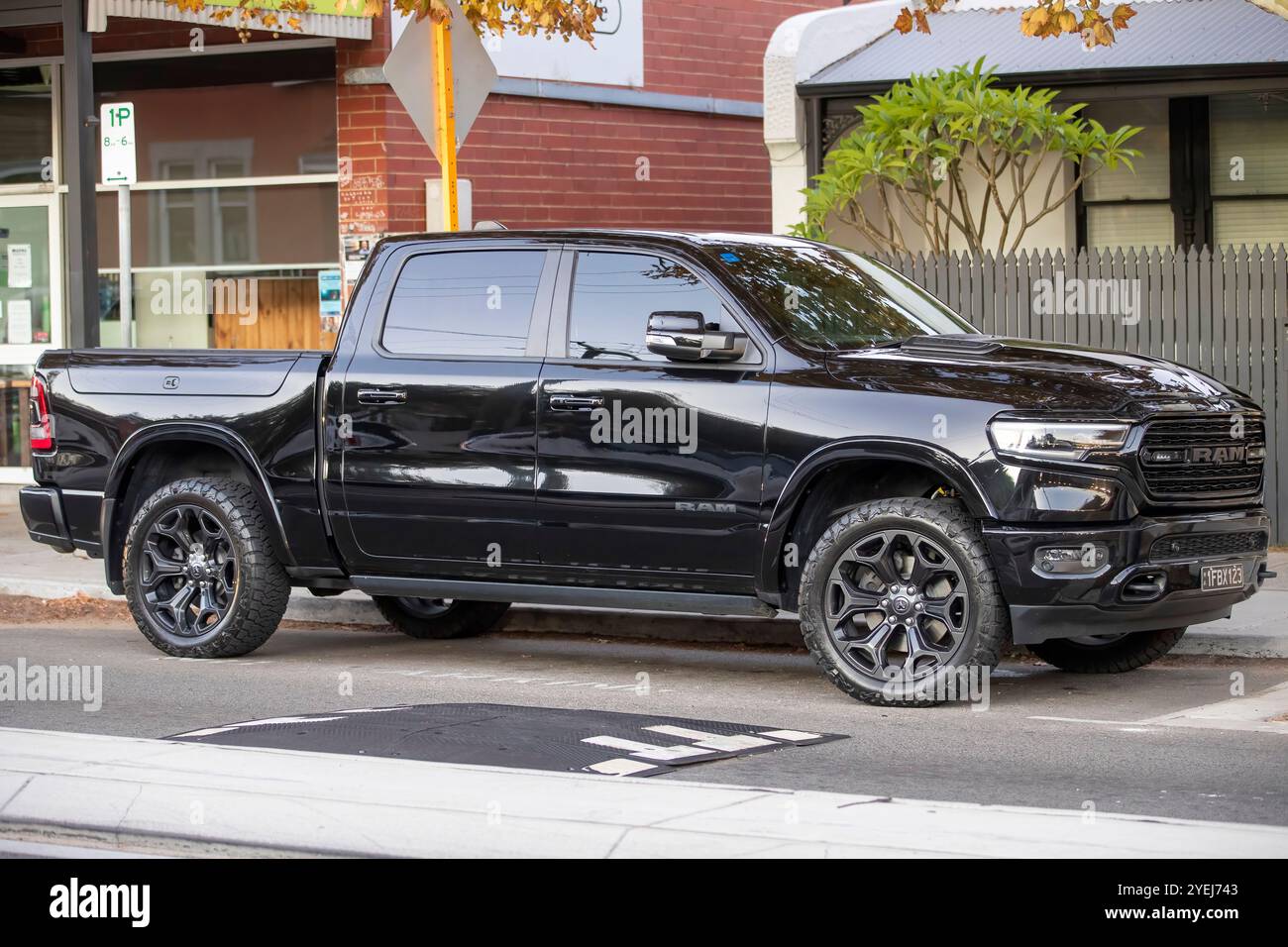 Ein schwarzer RAM 1500 Pickup-Truck, der auf einer Vorstadtstraße geparkt ist, mit getönten Fenstern und Geländereifen, mit einem Backsteingebäude. Stockfoto