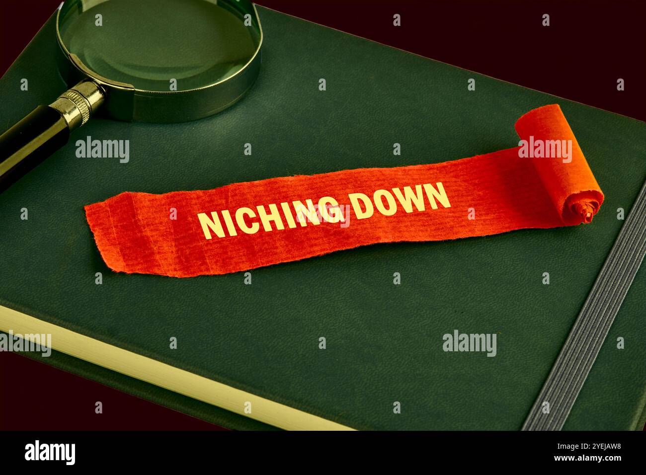 Das Konzept des Info-Geschäfts. Der Text von NICHING DOWN ist auf einem Stück aufgeklappten roten Zettel, Papier auf einem grünen Buch geschrieben. Gesättigte Farben. Stockfoto