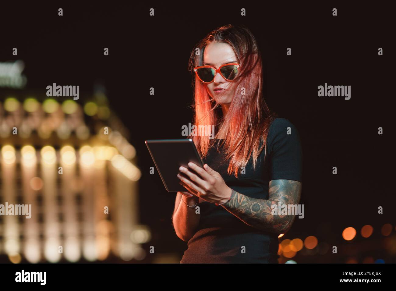 Schöne rothaarige Frau mit Brille, die draußen nachts ein digitales Tablet benutzt Stockfoto