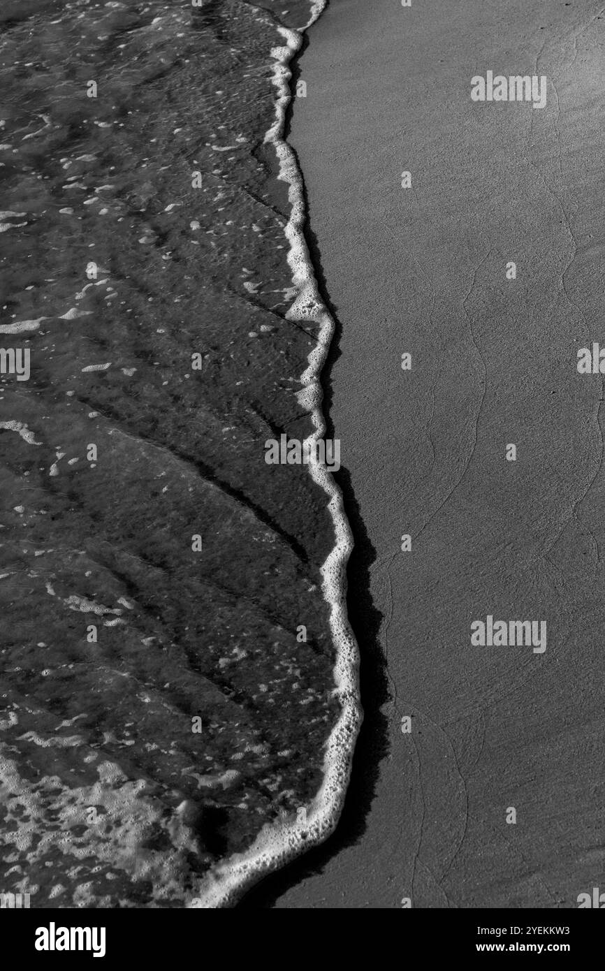 Morgenwellen am Sandy Beach: Kontrast zwischen nasser und trockener Oberfläche an der Küste. Schwarzweiß. Griechenland 2024 Stockfoto