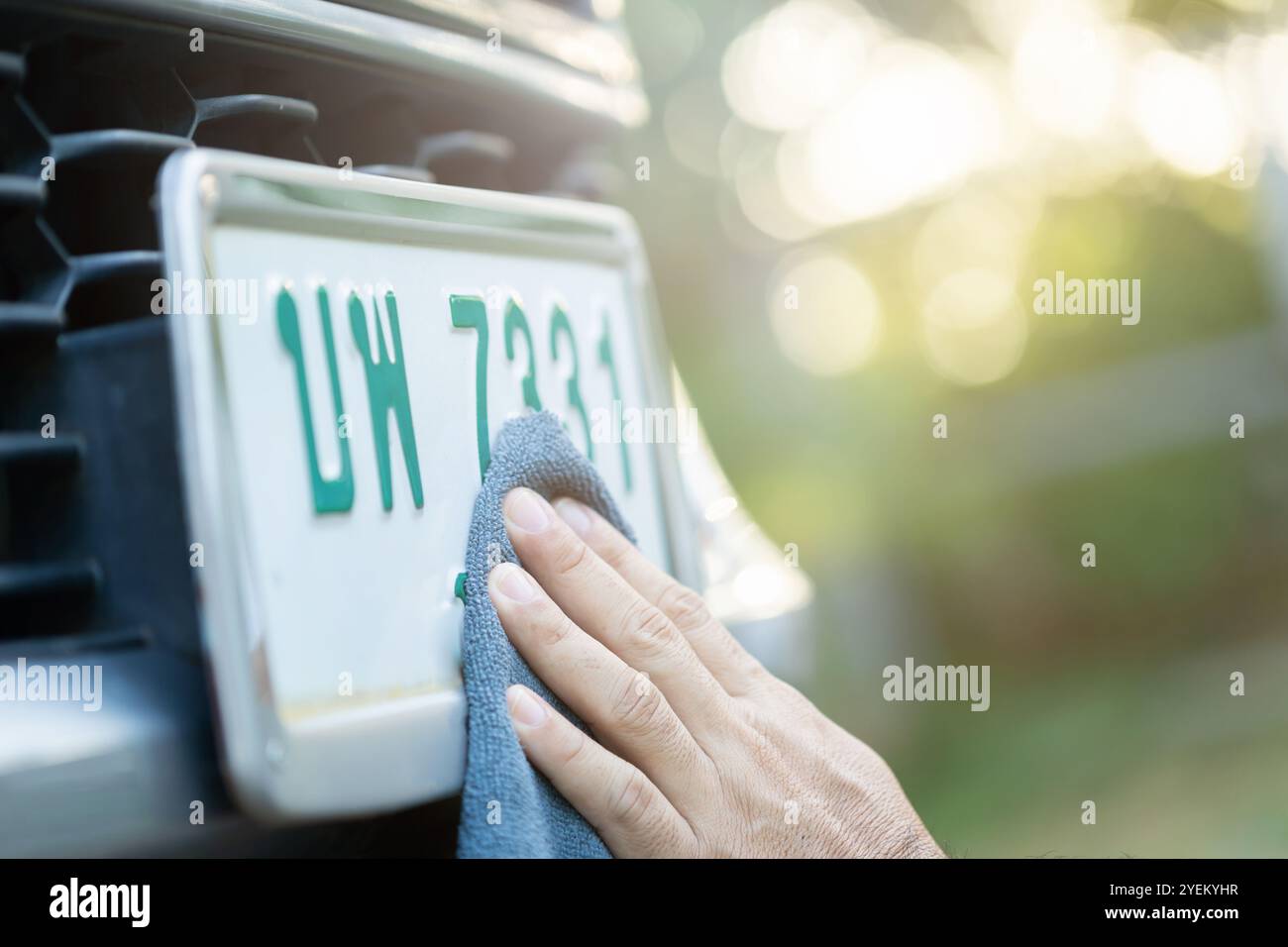 Der Autobesitzer wischt vorsichtig sein Kennzeichen ab, was die thailändischen Überzeugungen in Glückszahlen auf den Fahrzeugschildern und die Aufmerksamkeit, die auf die Wartung gelegt wird, widerspiegelt Stockfoto