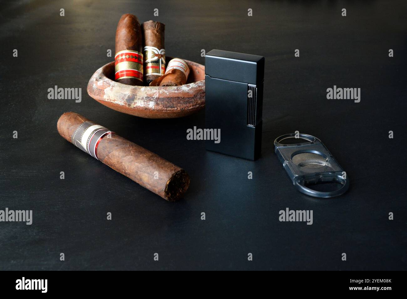 Eine Zigarre vor einem Aschenbecher mit einem Feuerzeug und einem Zigarrenschneider. Stockfoto