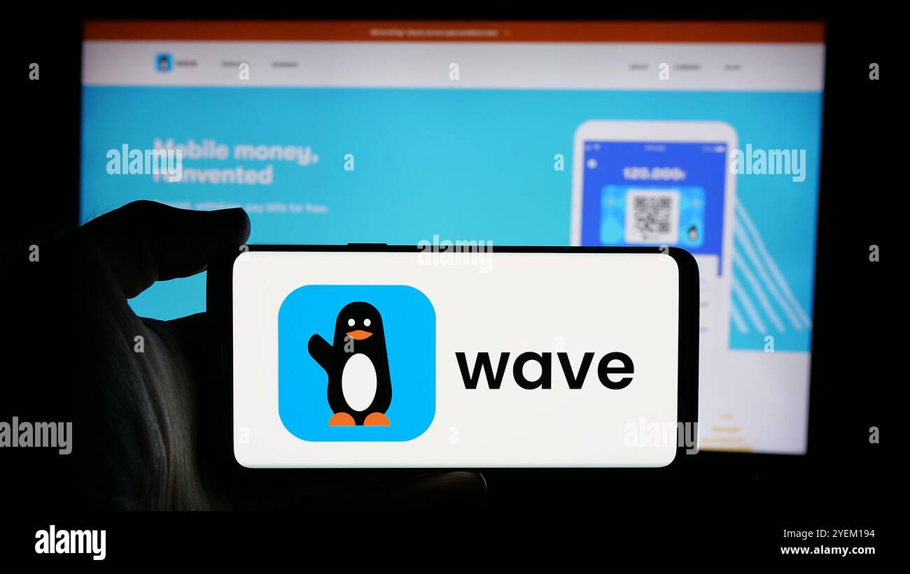Person, die ein Mobiltelefon mit dem Logo des sengalesischen Unternehmens Wave Mobile Money Inc. Auf dem Bildschirm vor der Unternehmenswebseite hält. Schwerpunkt auf dem Display des Telefons. Stockfoto