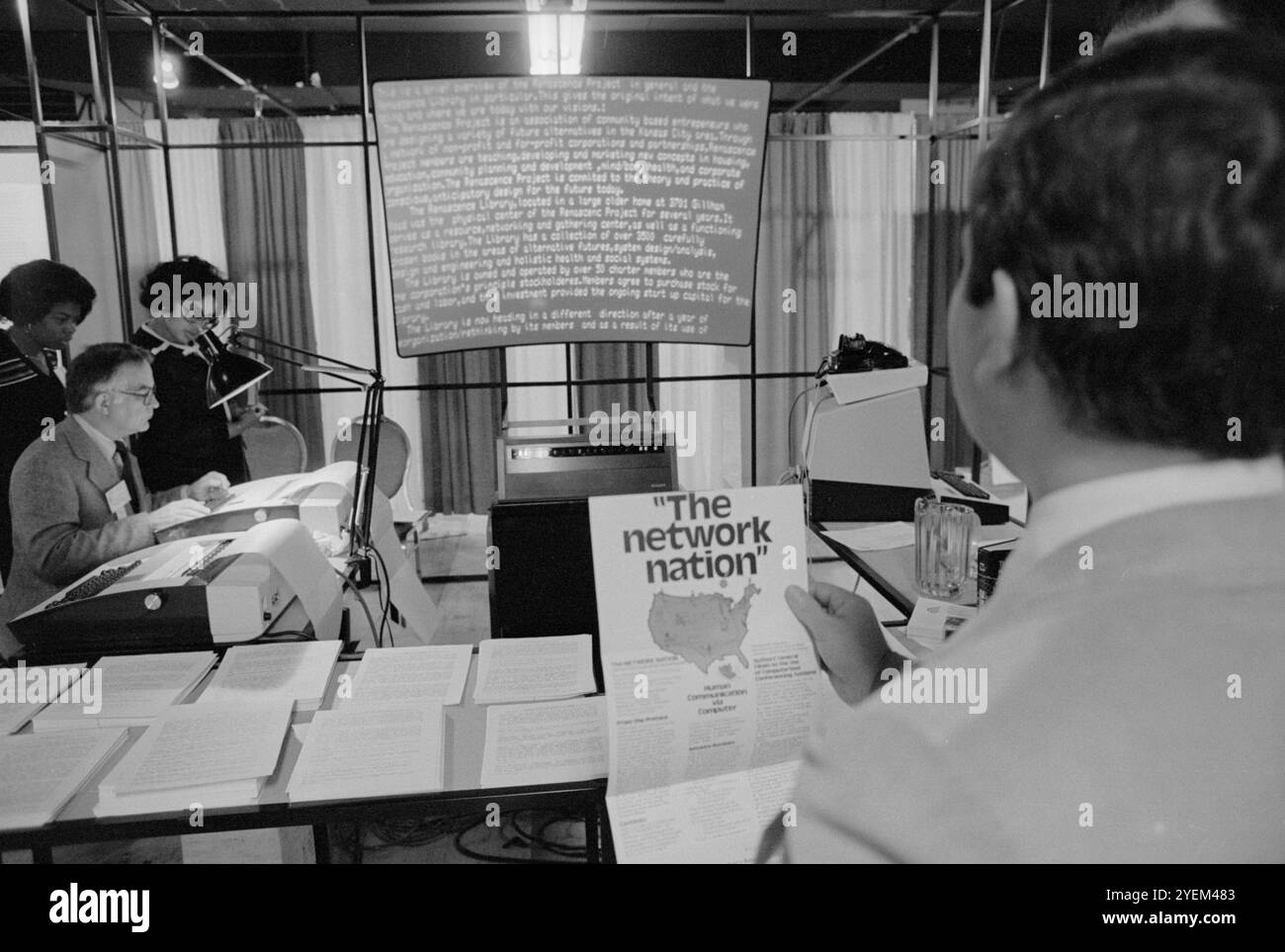 Ein Mann, der sich eine Broschüre „vernetzte Nation“ anschaut und ein anderer Mann, der Computer benutzt, während andere auf einer Ausstellung (?) auf der Konferenz des Weißen Hauses über Library and Information Services in Washington, D.C. USA schauen. 16. November 1979 Stockfoto
