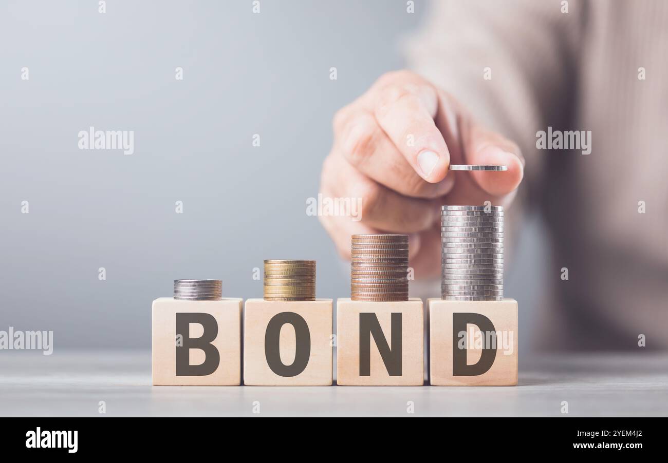 Wenn Sie Münzen von Hand auf einen Holzblock mit der Aufschrift „BOND“ stapeln, spiegelt das Bild das stetige und strukturierte Wachstum wider, das mit Anleiheninvestitionen verbunden ist Stockfoto