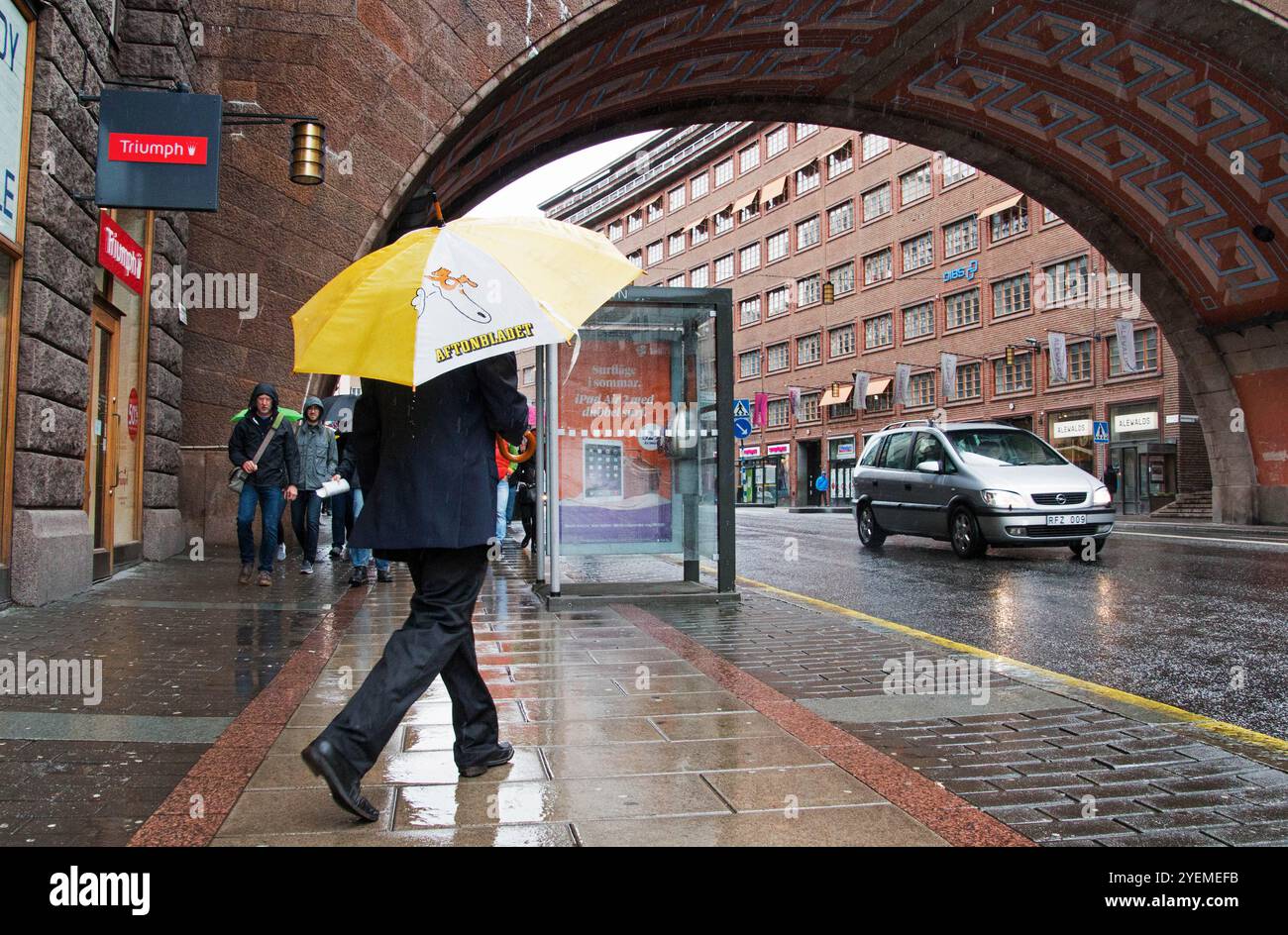 Das tägliche Leben in Kungsgatan in Stockholm, Schweden. Jemand mit einem Regenschirm, der an einer Telefonzelle vorbeifährt. Stockfoto