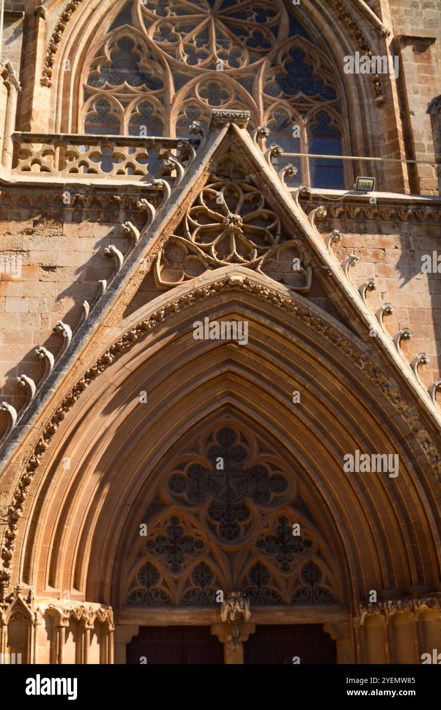 Ein atemberaubender gotischer Eingang zeigt kunstvolle Steinschnitzereien und komplizierte Details, die von Sonnenlicht warm beleuchtet werden. Stockfoto