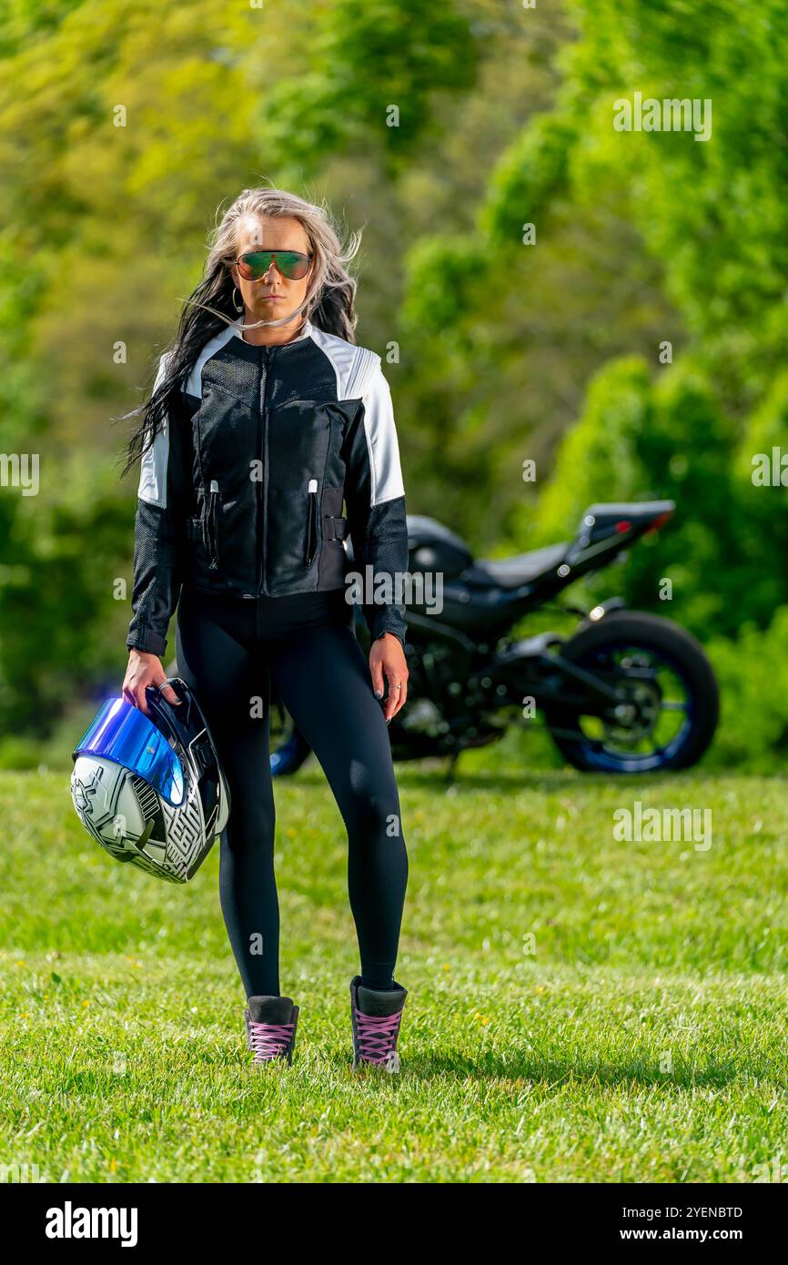 Eine umwerfende Frau posiert selbstbewusst neben ihrem leistungsstarken Motorrad. Mit einem heftigen Blick und einer ausgeglichenen Haltung strahlt sie Kraft und Leidenschaft aus Stockfoto